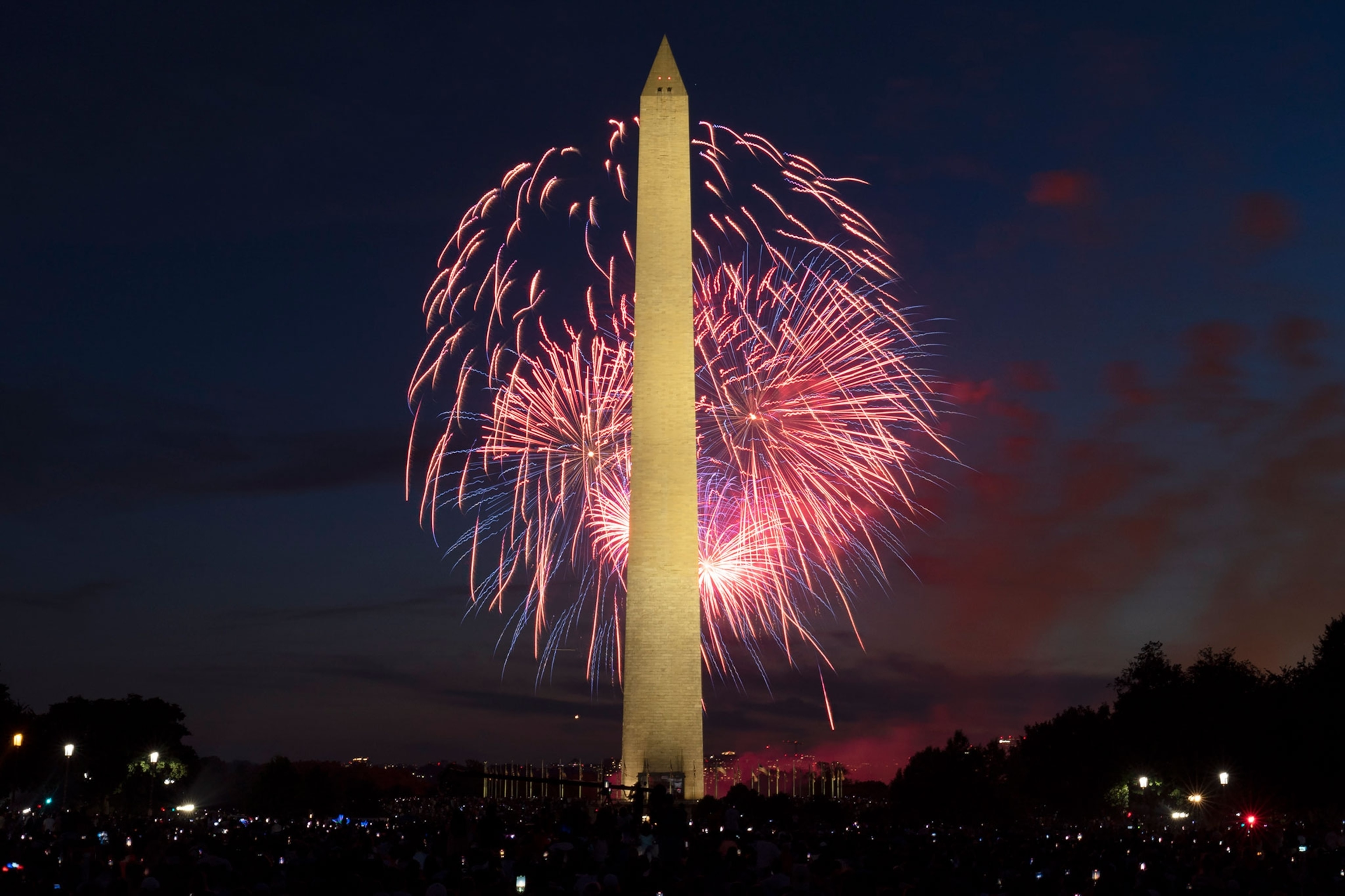 Fireworks go off behind the lit up Washington Monument at night.