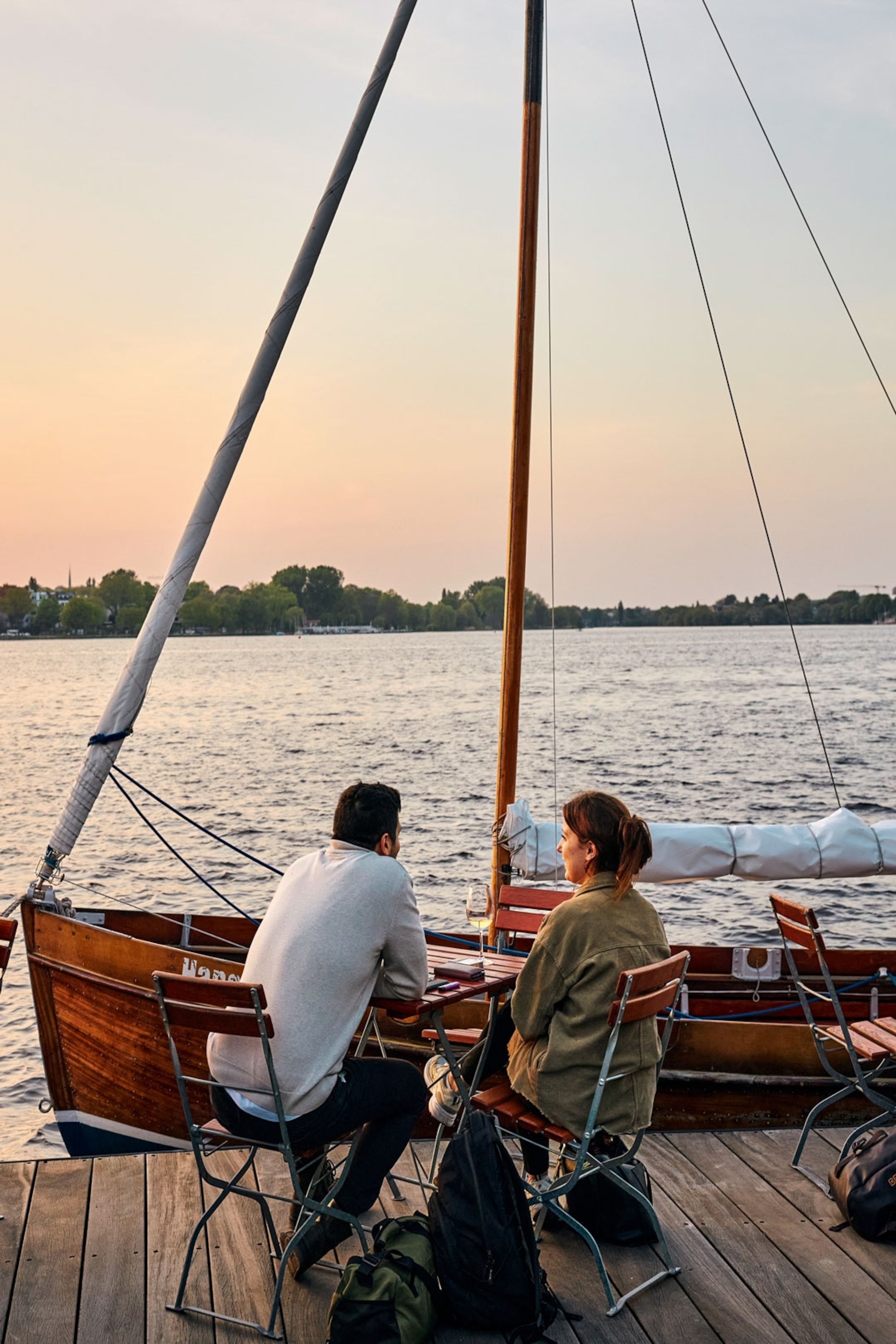 A couple sit at table overlooking a lake at sunset.
