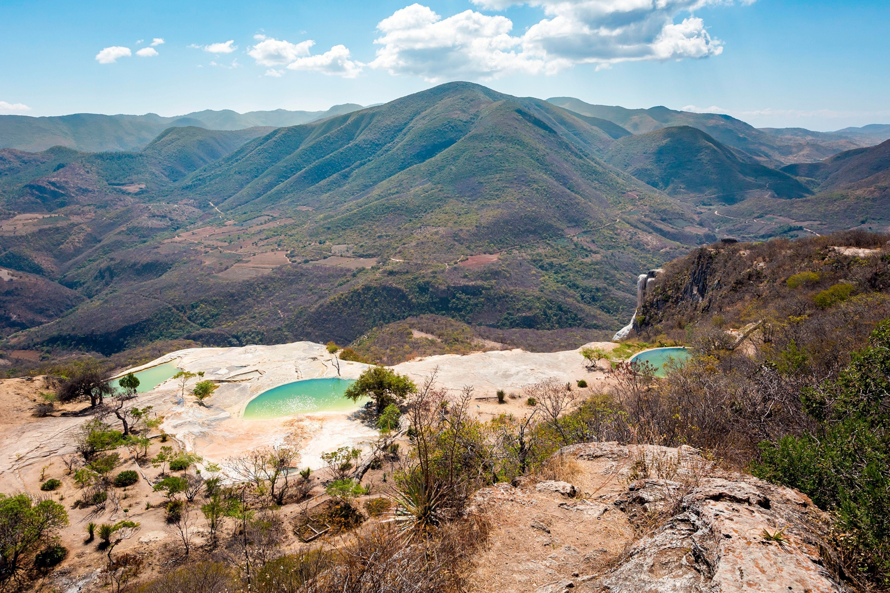 A rocky, mountainous landscape with natural pools amid dry bushes.