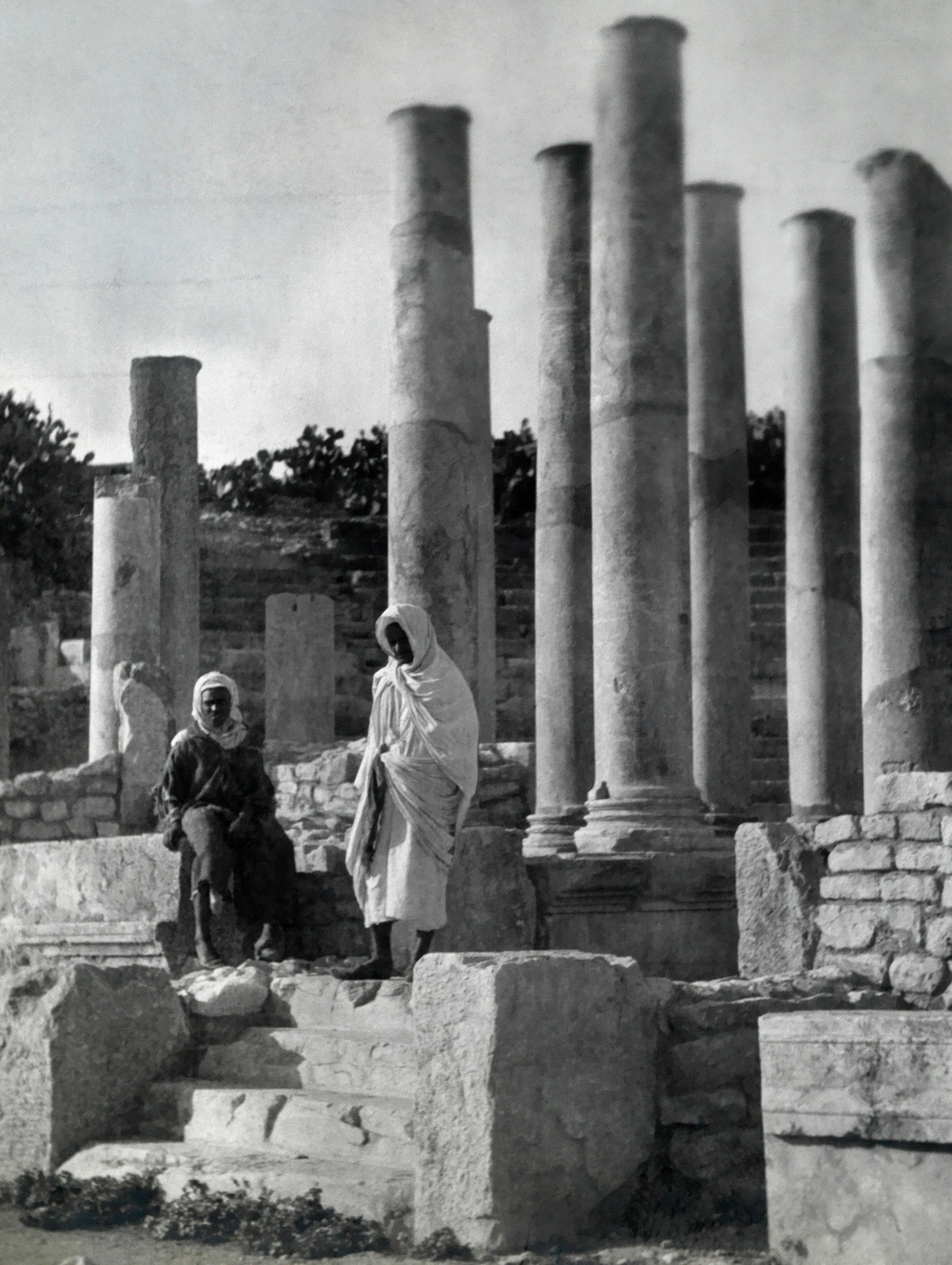 People stand among the Roman ruins in the capital city of Tunis, Tunisia in 1909 in a black and white photo