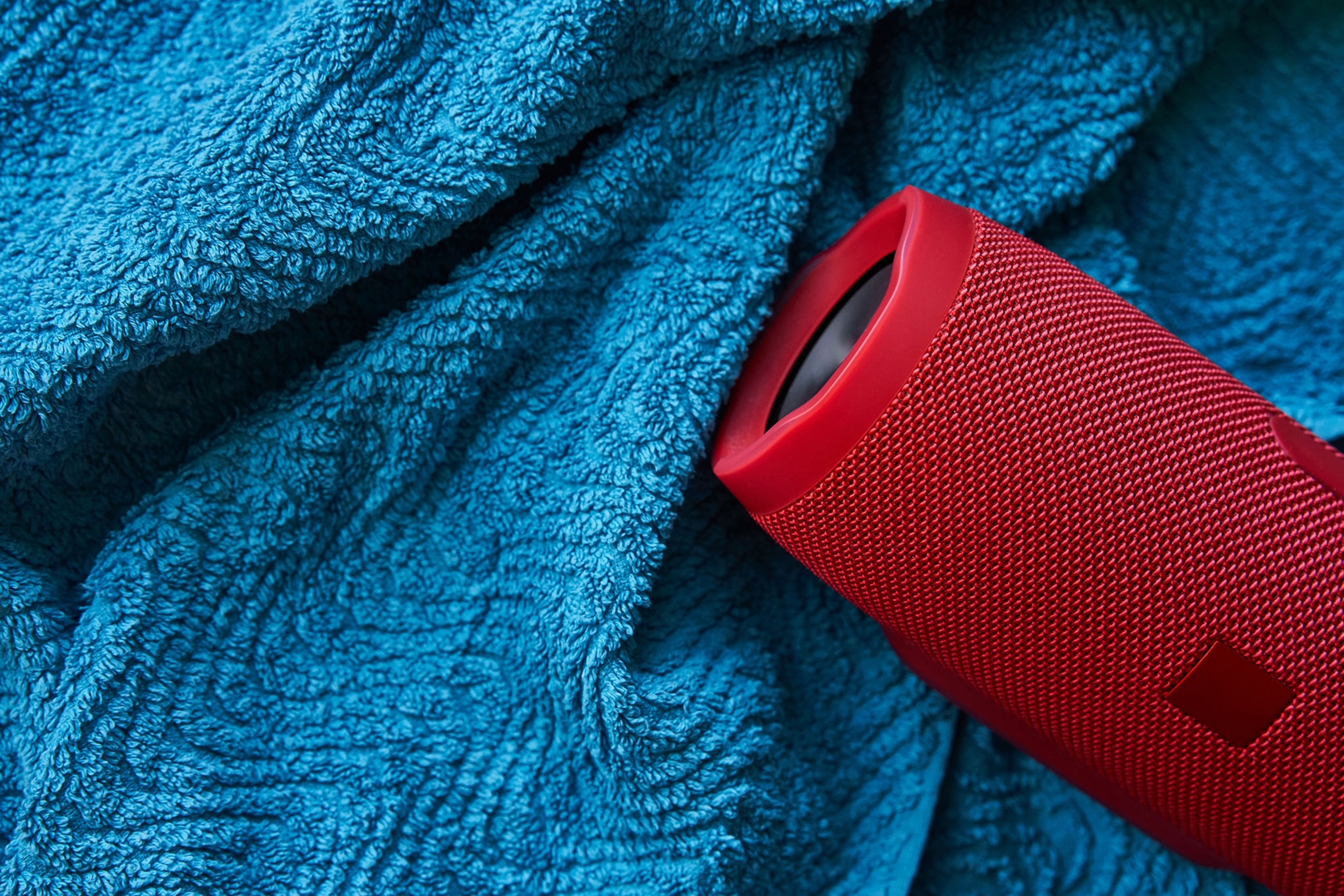 A small red speaker sits on top of a blue towel.