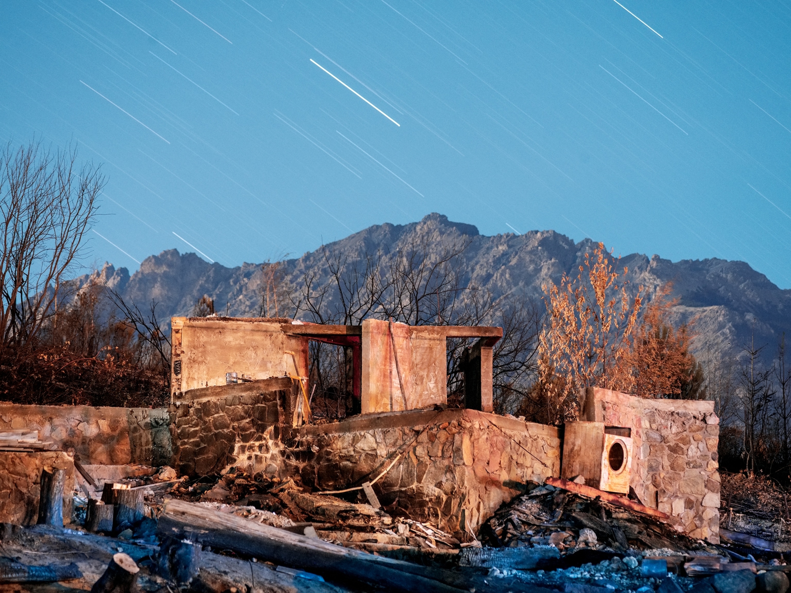 the charred remains of a house seen at dusk with the blue sky and stars moving from a long exposure
