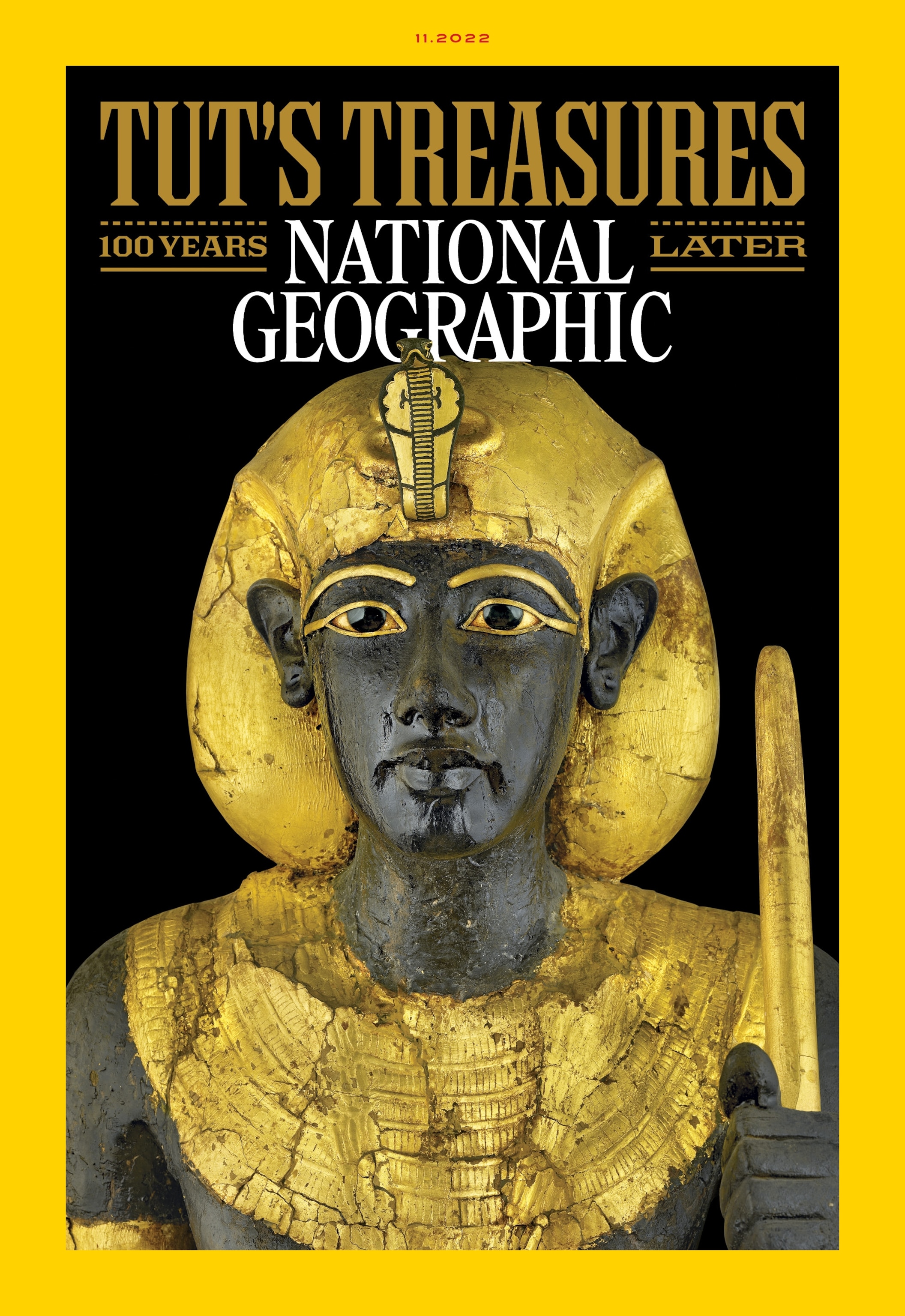 The November 2022 cover of National Geographic magazine, featuring a picture of a statue of a person on a black background. The statue has black skin, is wearing a gold headdress and collar, and holds a gold staff. The picture is surrounded by a yellow border an features the words "Tut's Treasures: 100 Years Later."