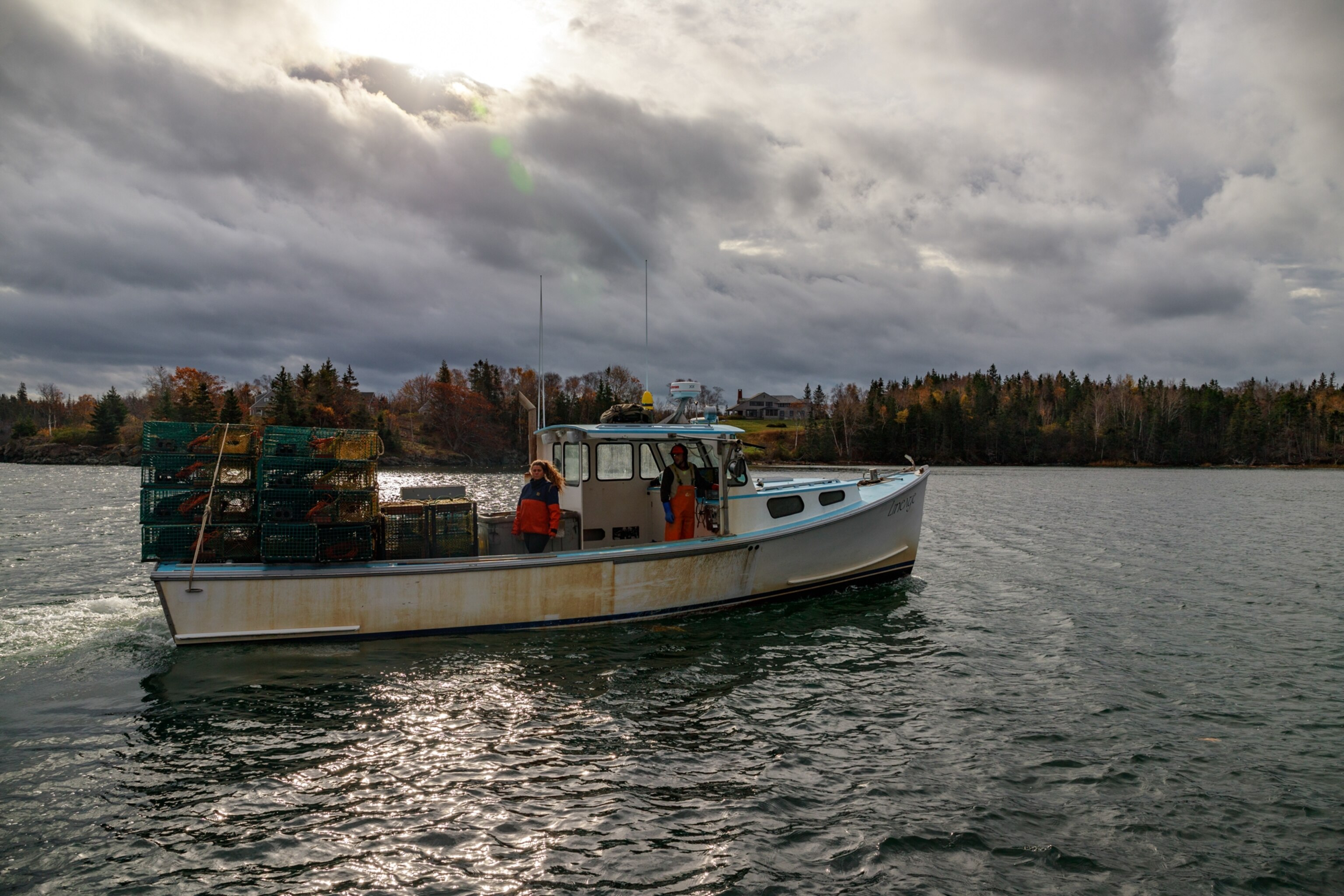 A fishing boat glides across the bay with lobster traps stacked on stern. North Haven Island, Maine, United States of America. 