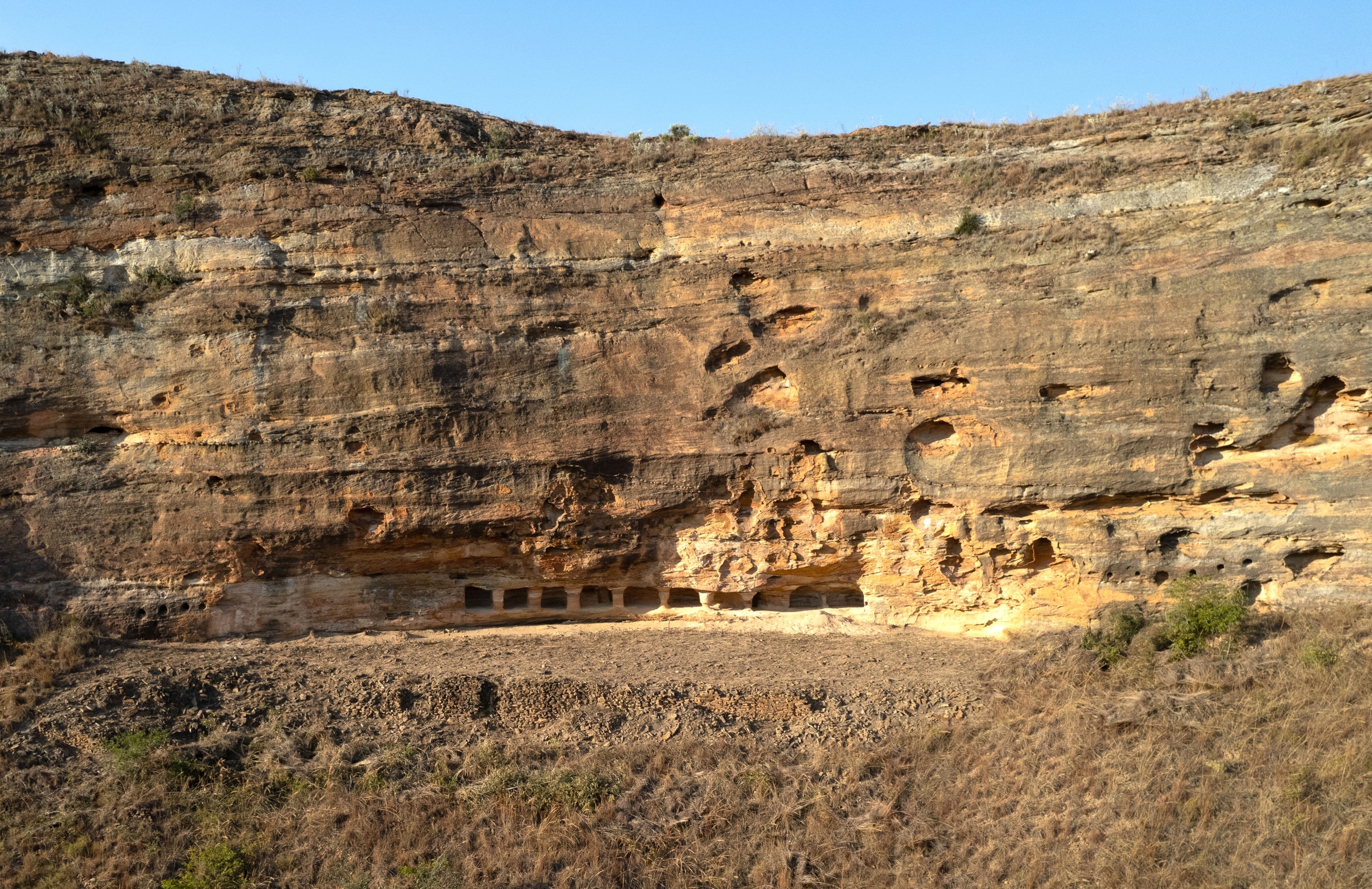 A pulled-away view of the quadrangular niches cut into a sheer sandstone rock wall.