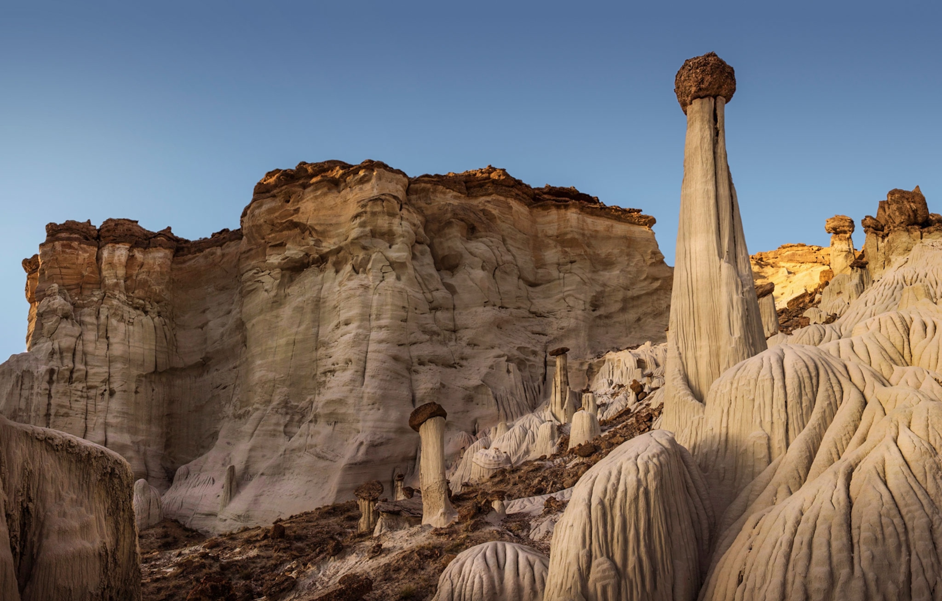Sandy, grey rock formations including tall structures with lighter bodies and darker, rocker tops, and sandy, greyish, rocks that have been carved into by water run off.
