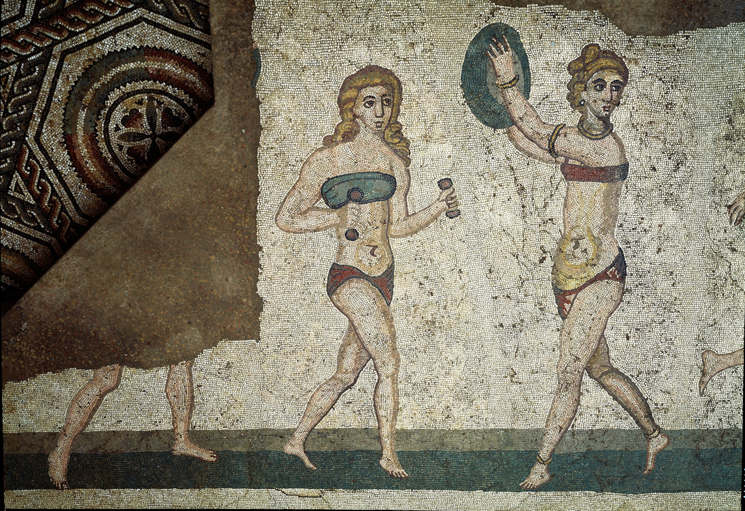 A photograph of a mosaic with young Romans engaged in physical exercises. They wear a loincloth around the kidneys and a strophium (ancetre of the bra) on the chest.