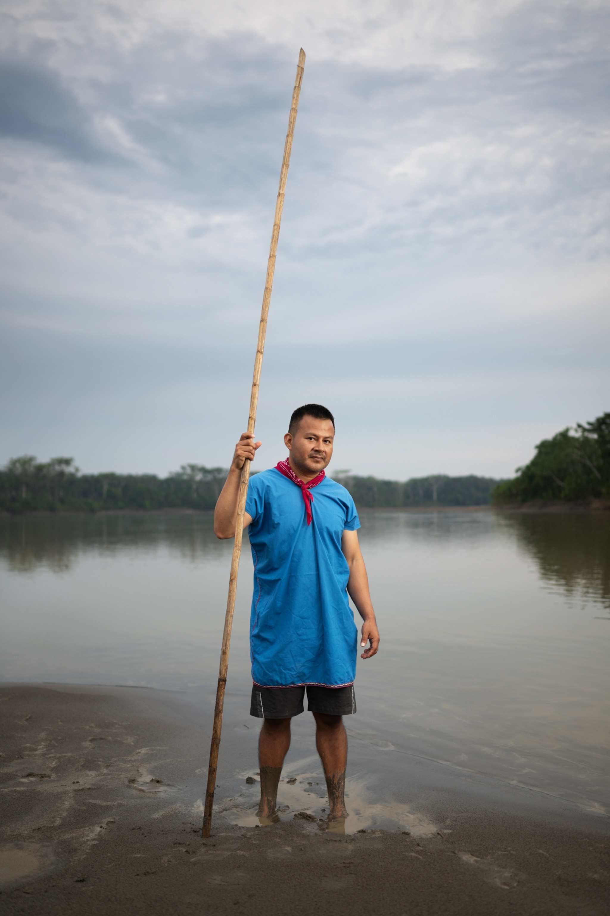 Hugo Lucitante is standing on the shore, feet in the muddied water, holding a stick twice his height.