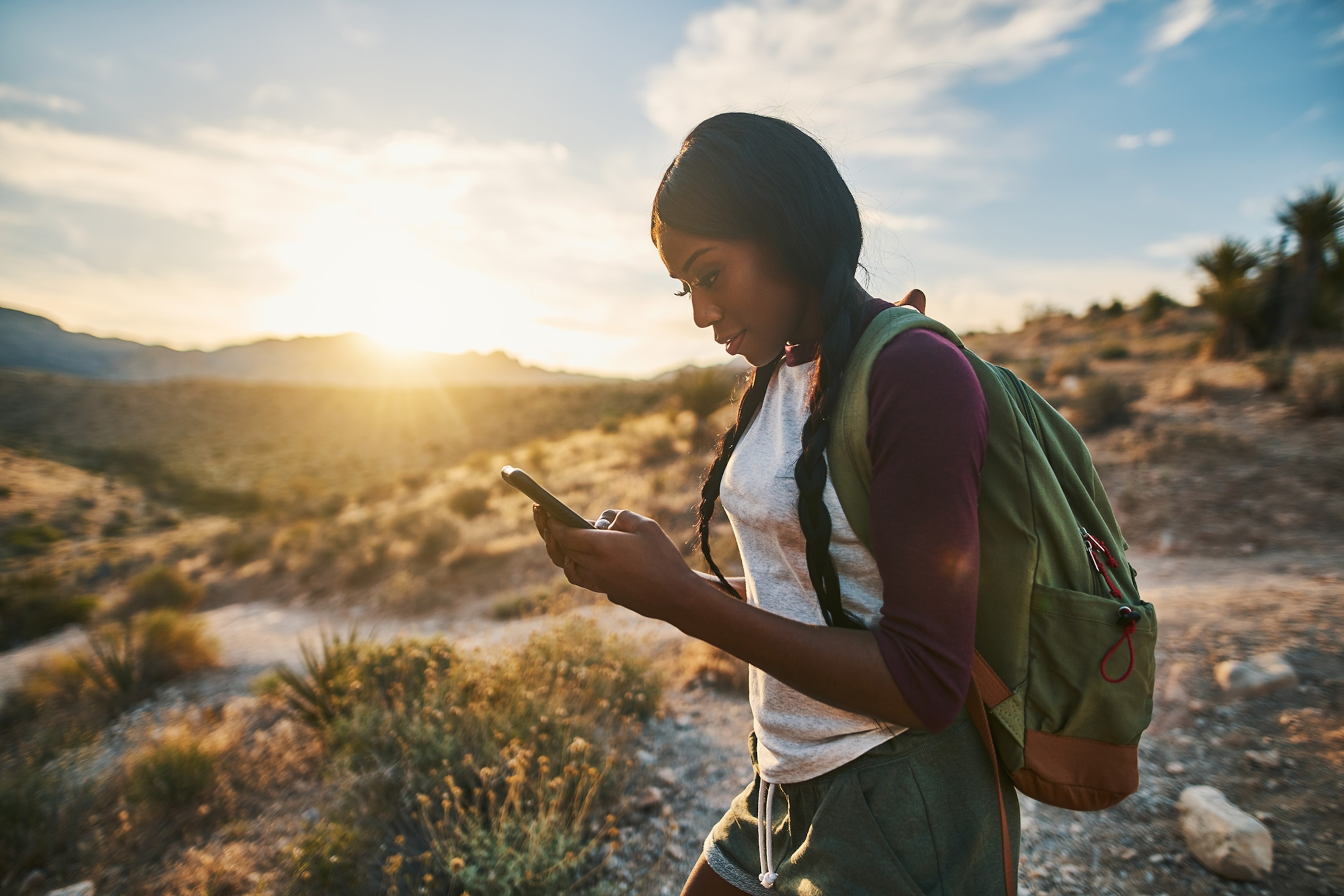 A woman with a backpack is looking at a phone while hiking in Red Rock Canyon, Nevada.