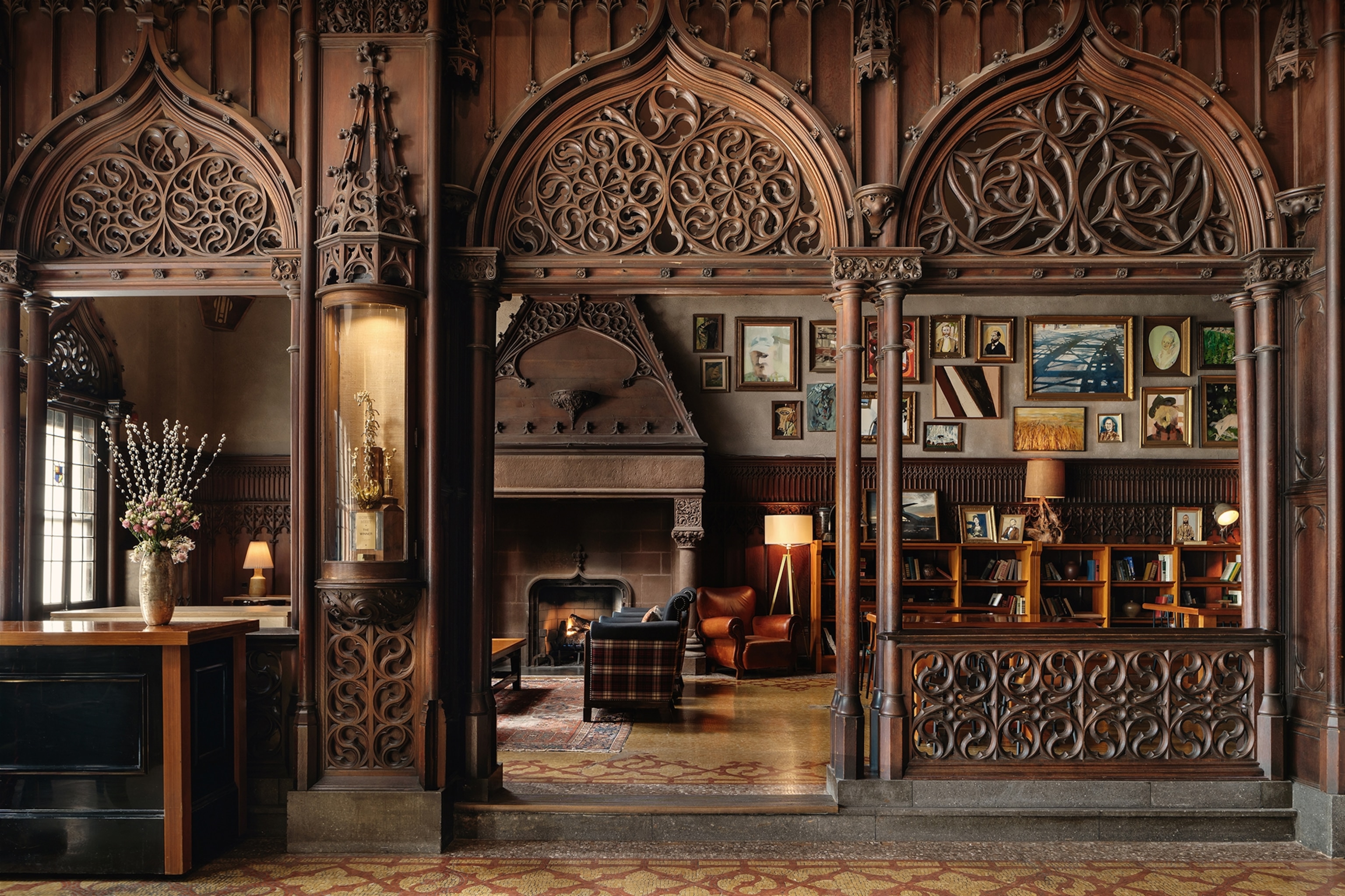 A view into a mosaic-tiled floor of a dark, wooden library with a structural room divider of carved wood.