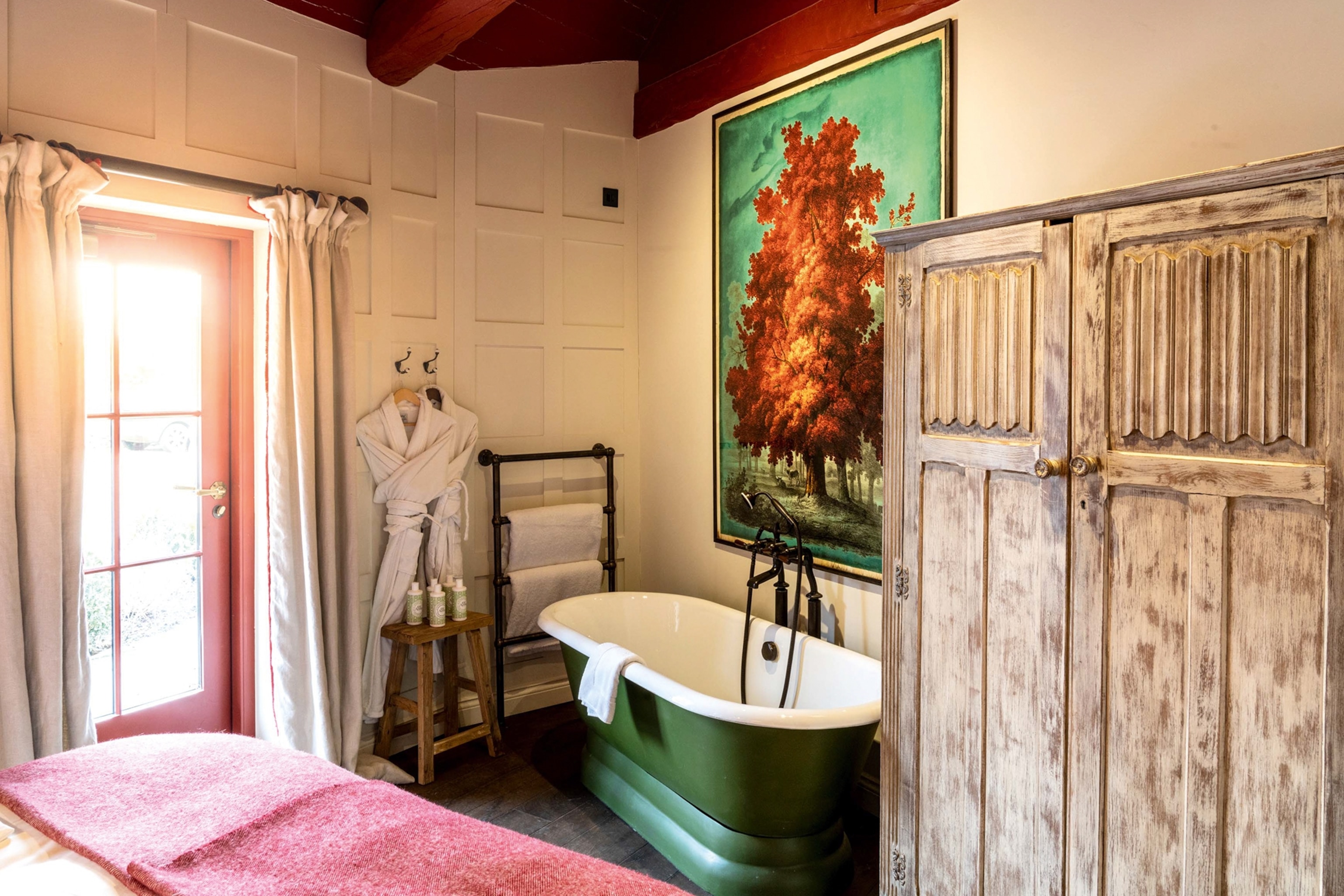 The interiors of a charming country bedroom with a beamed ceiling and a freestanding bathtub at the foot of the bed.