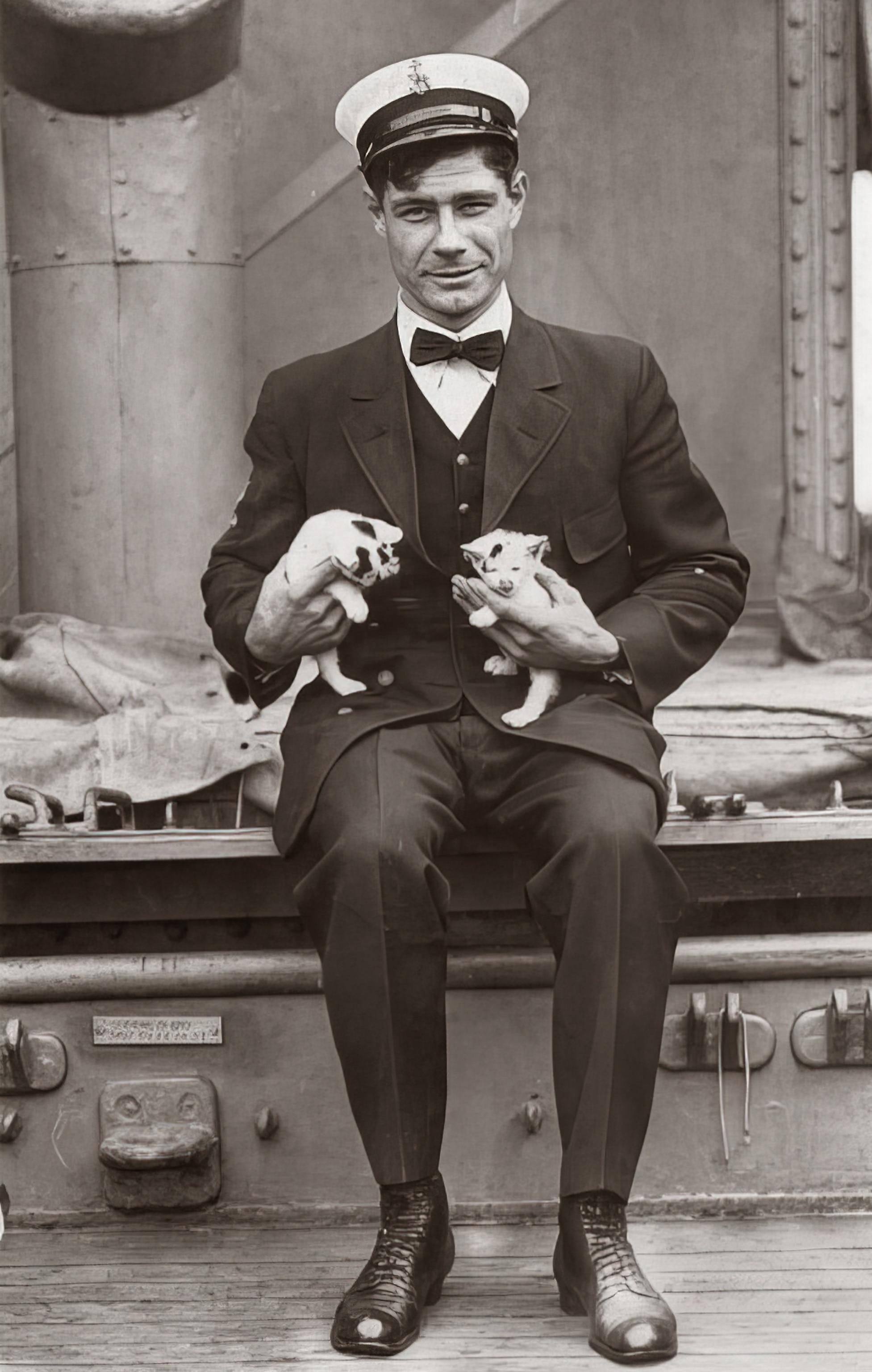 Photo of sailor seated on deck with two kittens on lap