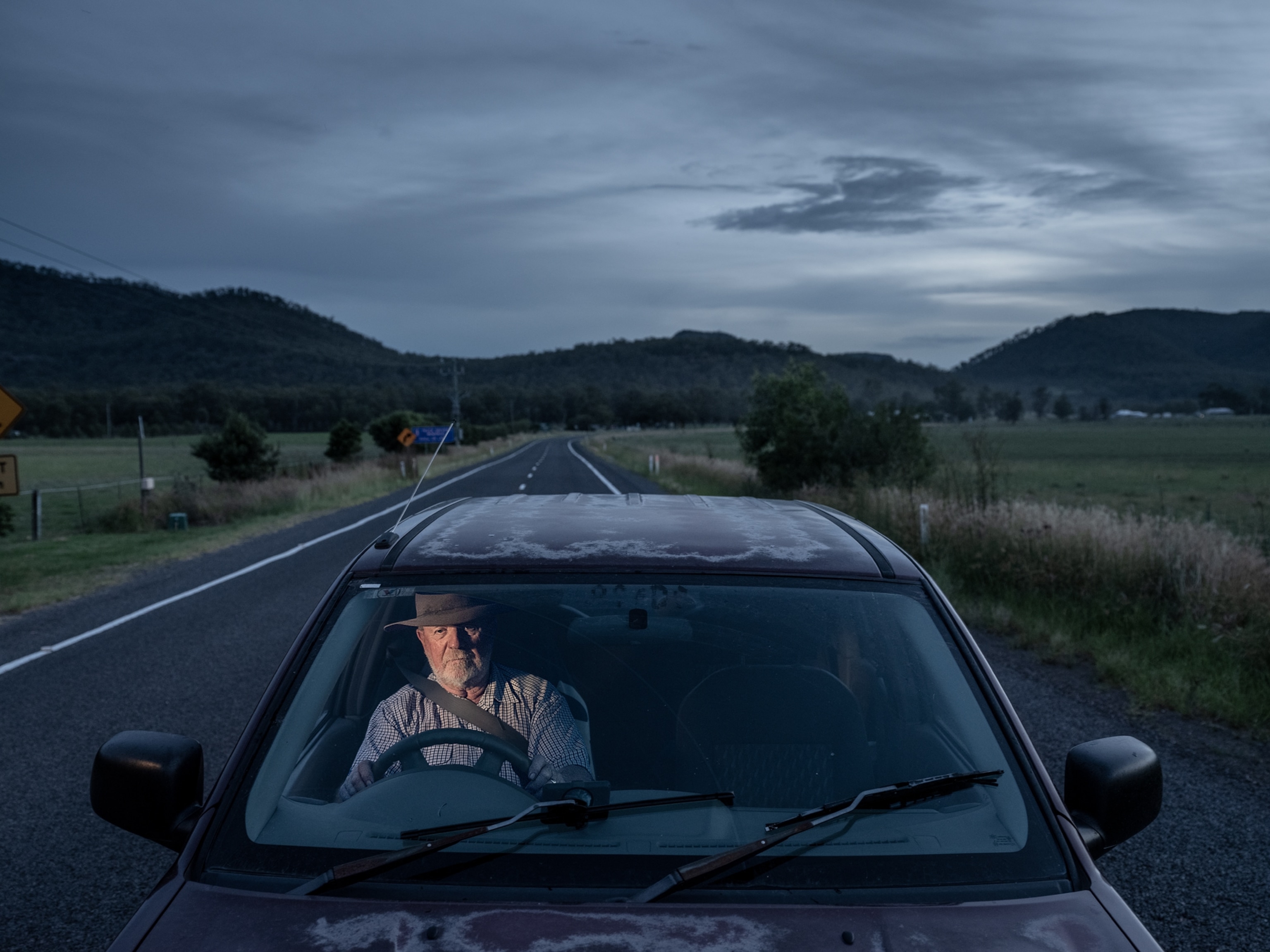 man sitting in a car under gray skies in dusk.