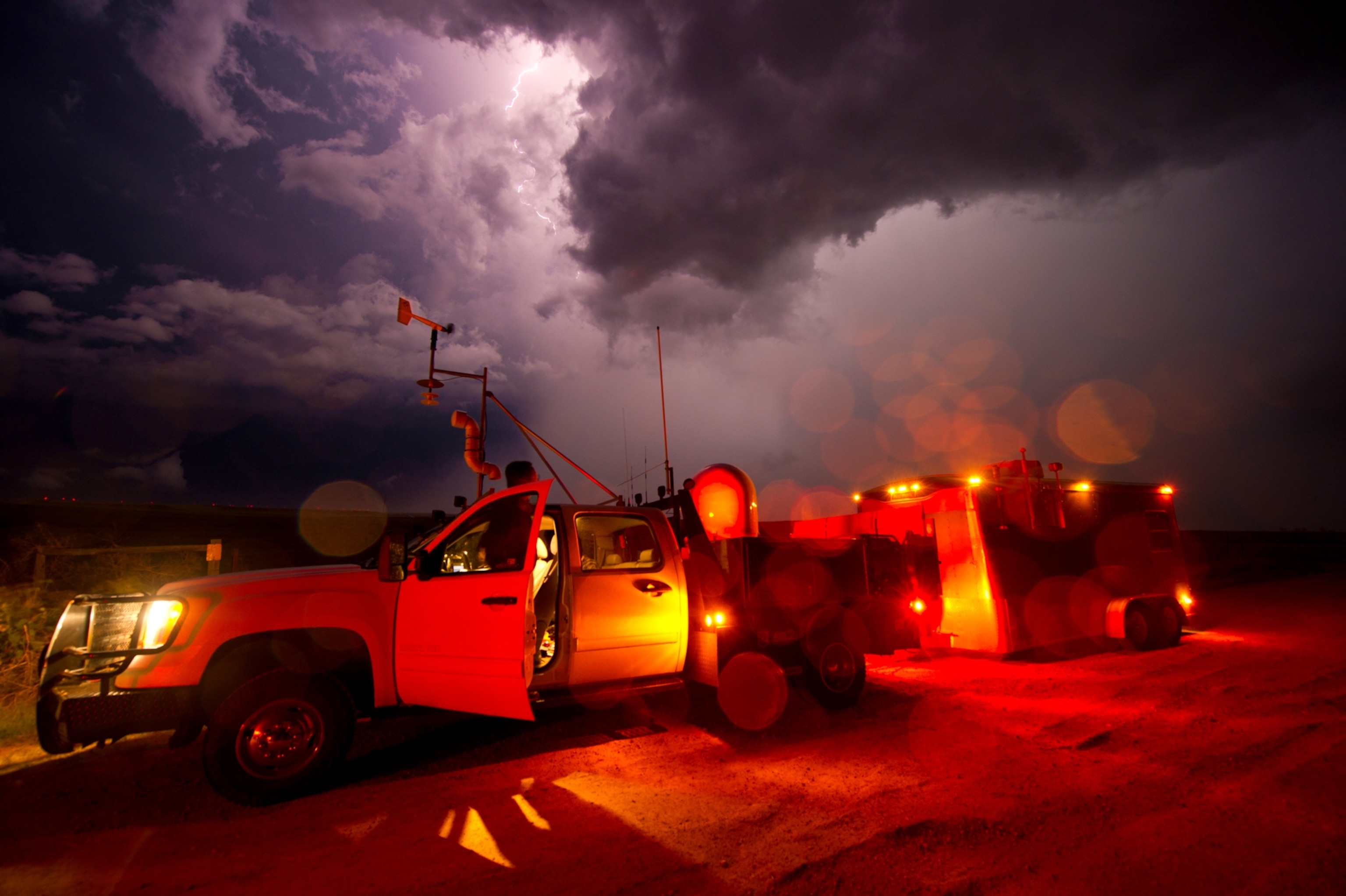 Lightning filling the sky above a pickup truck and trailer that have been equipped for storm chasing.