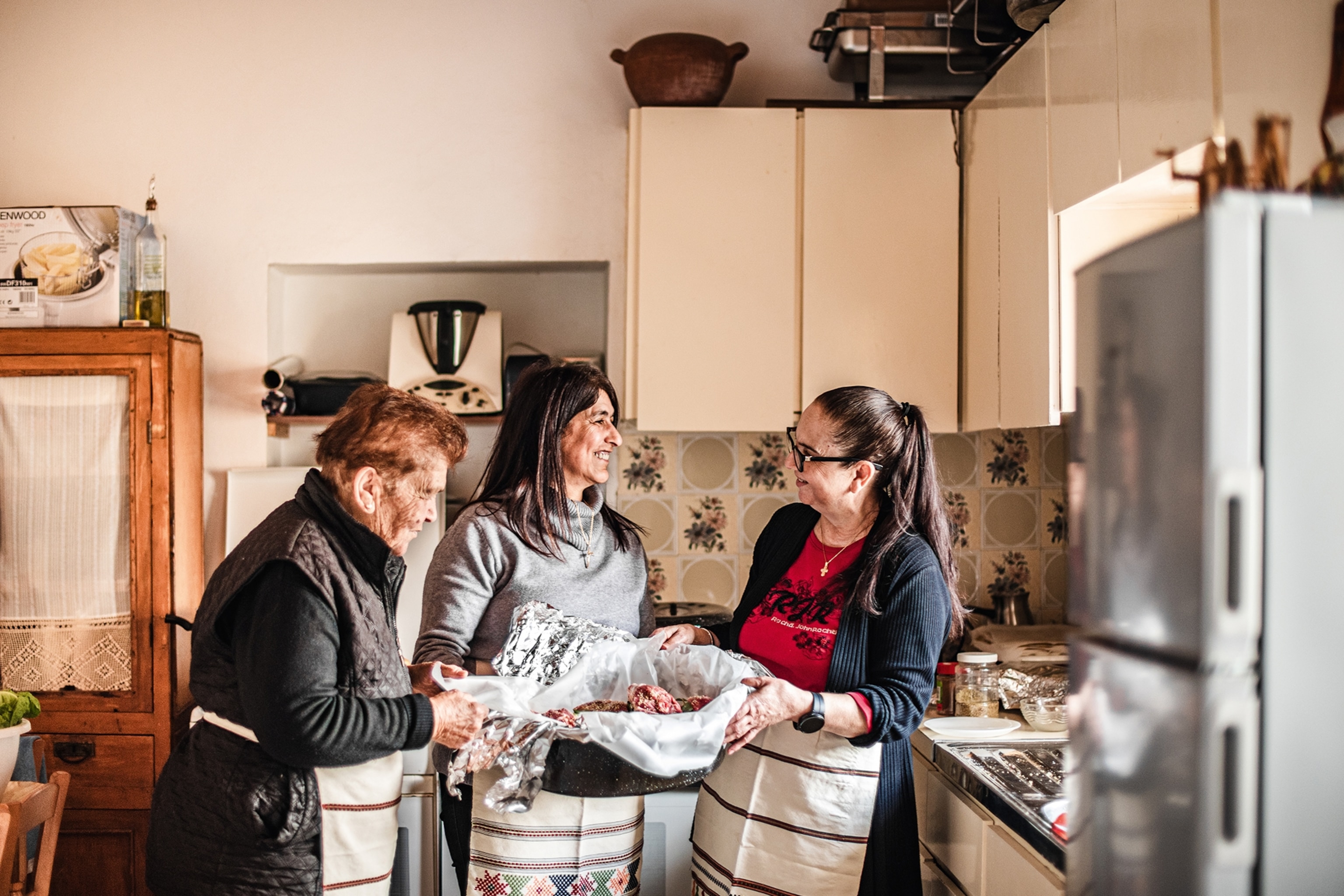 Women standing in a kitchen holding a pot of raw meat ready to be cooked