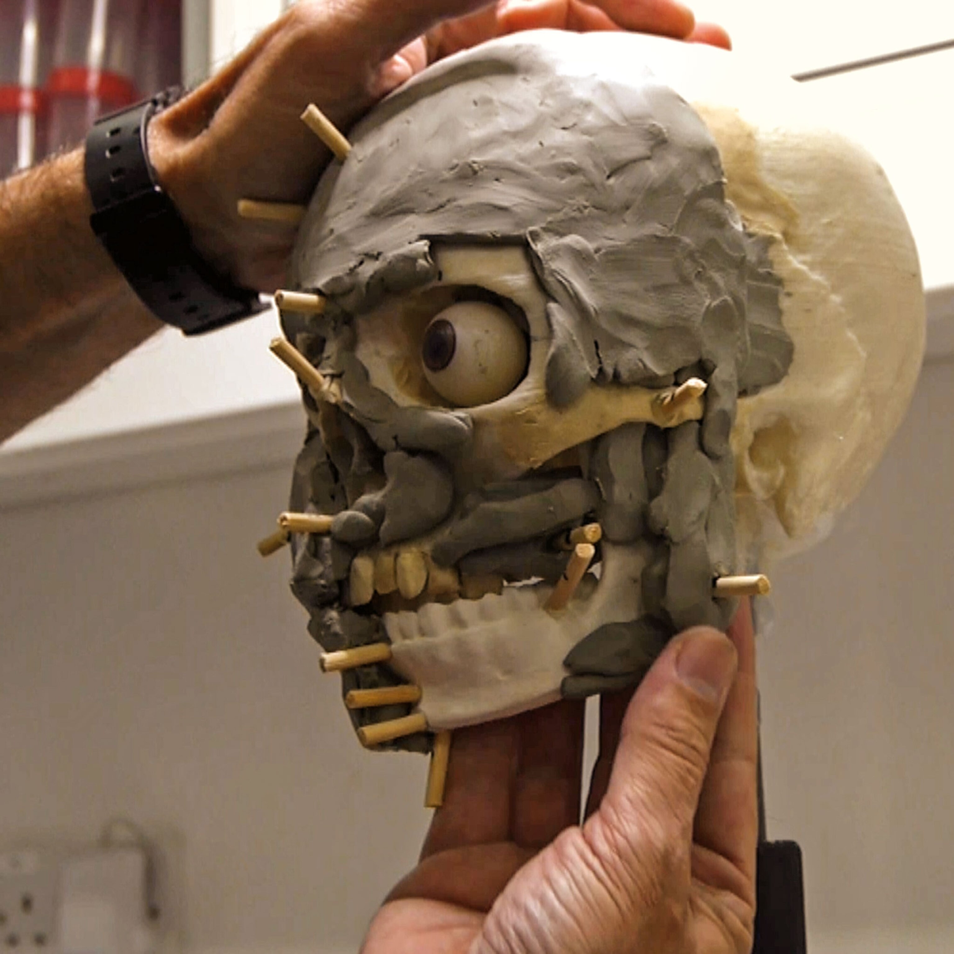 hands sculpting a skull with clay and a fake eyeball