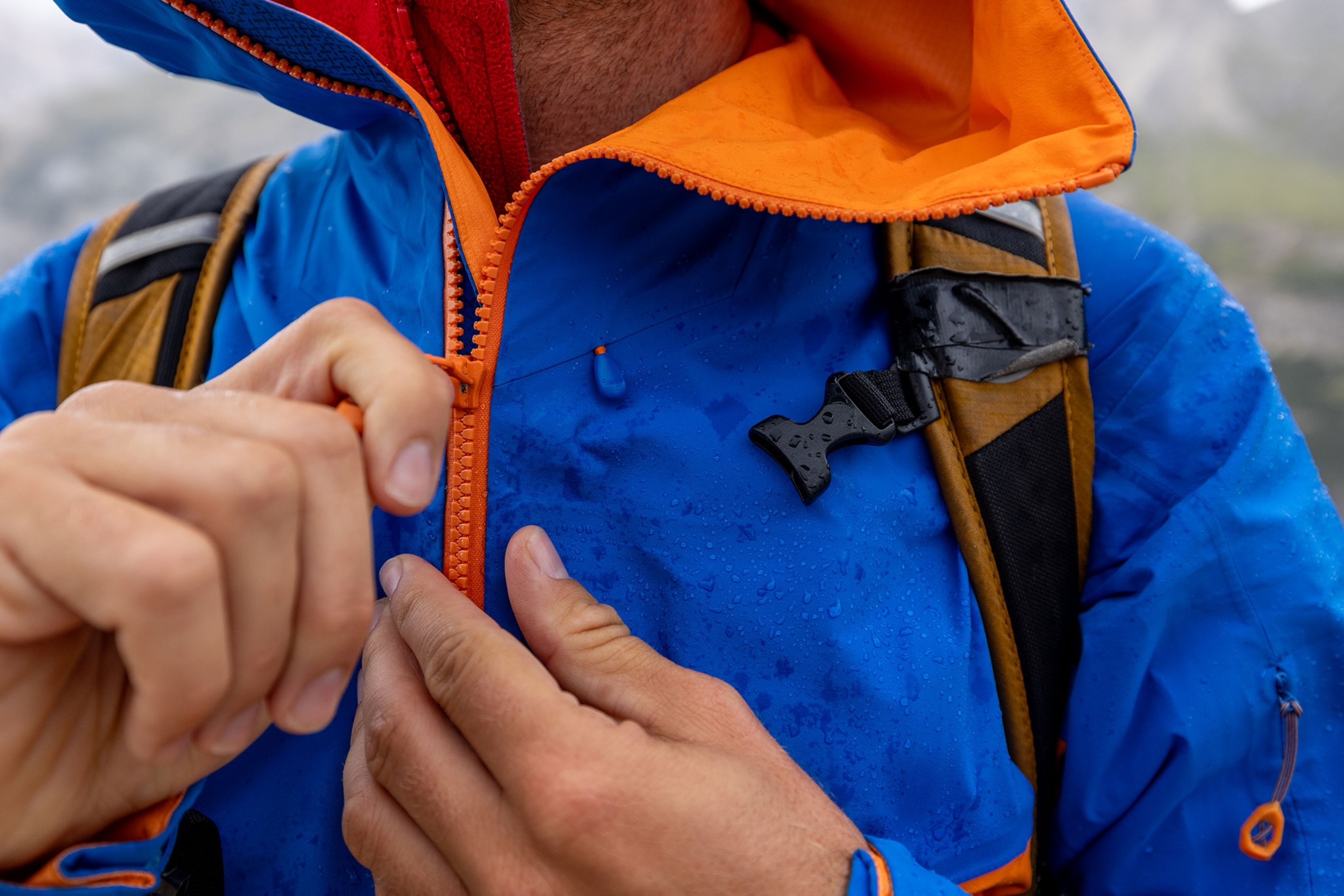 Person zipping up blue and orange rain jacket.