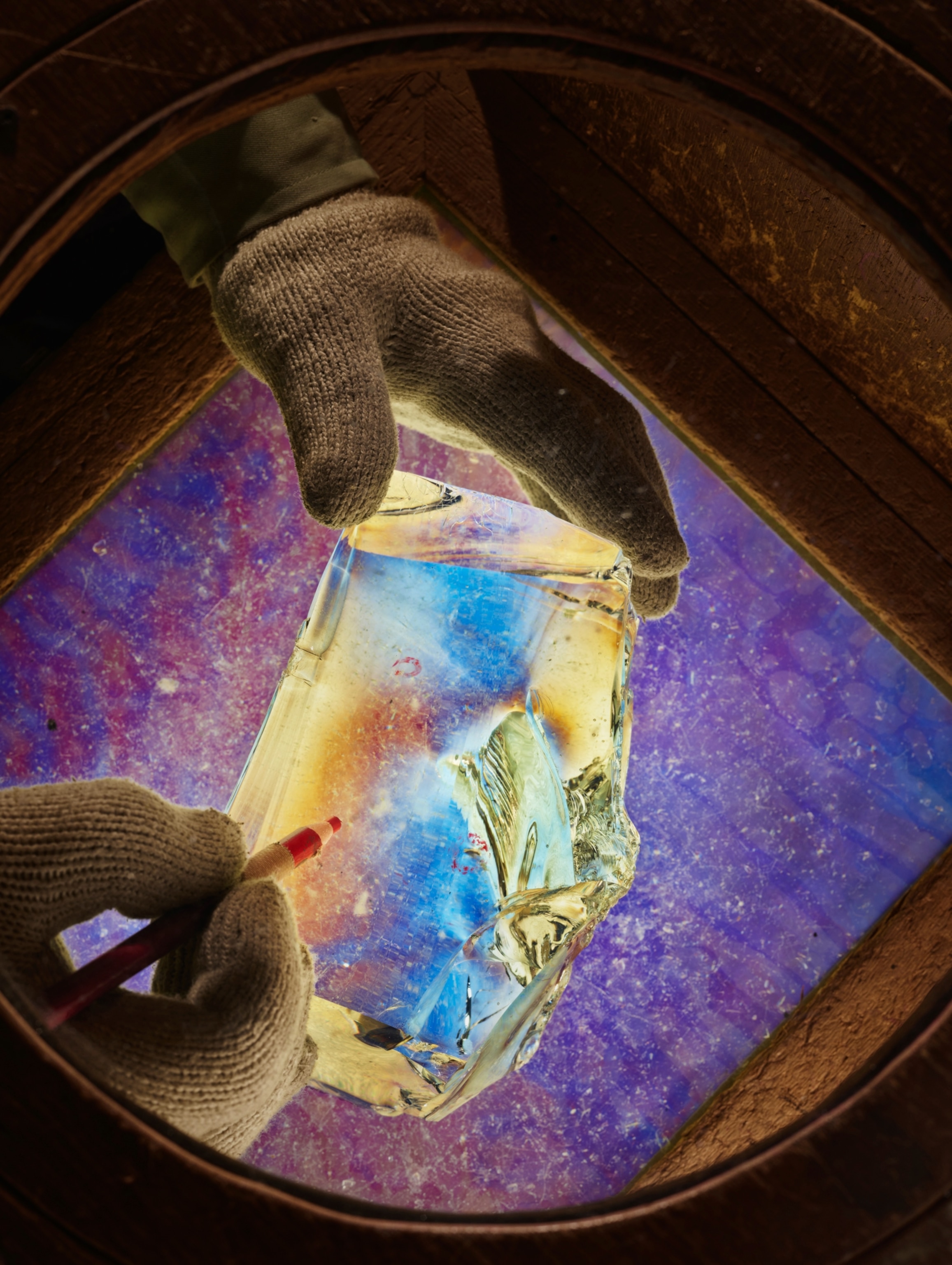two gloved hands holding a piece of glass under a magnifier and marks it with a pen.