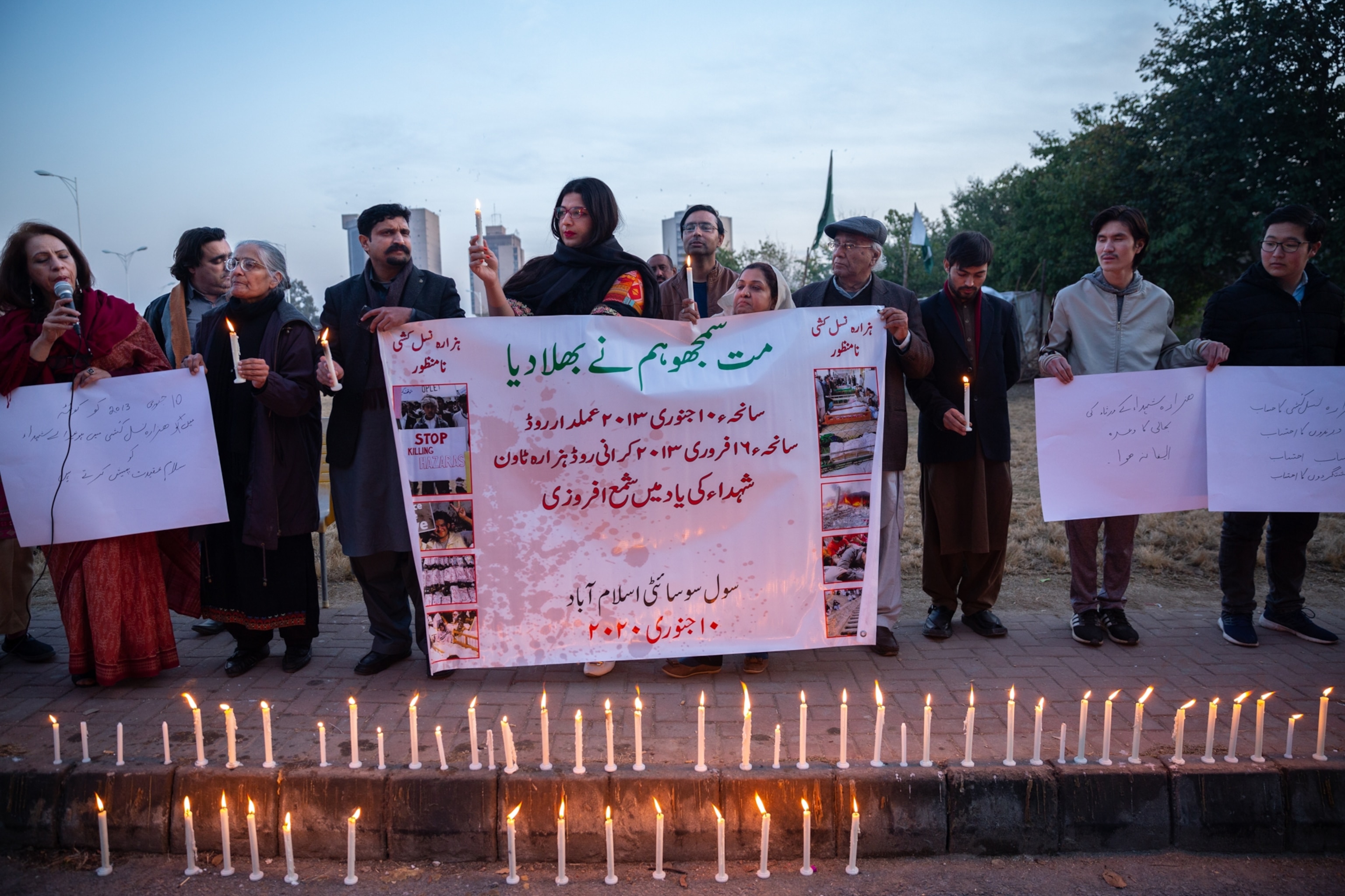 a group of people with a banner stand in front of candles at dusk