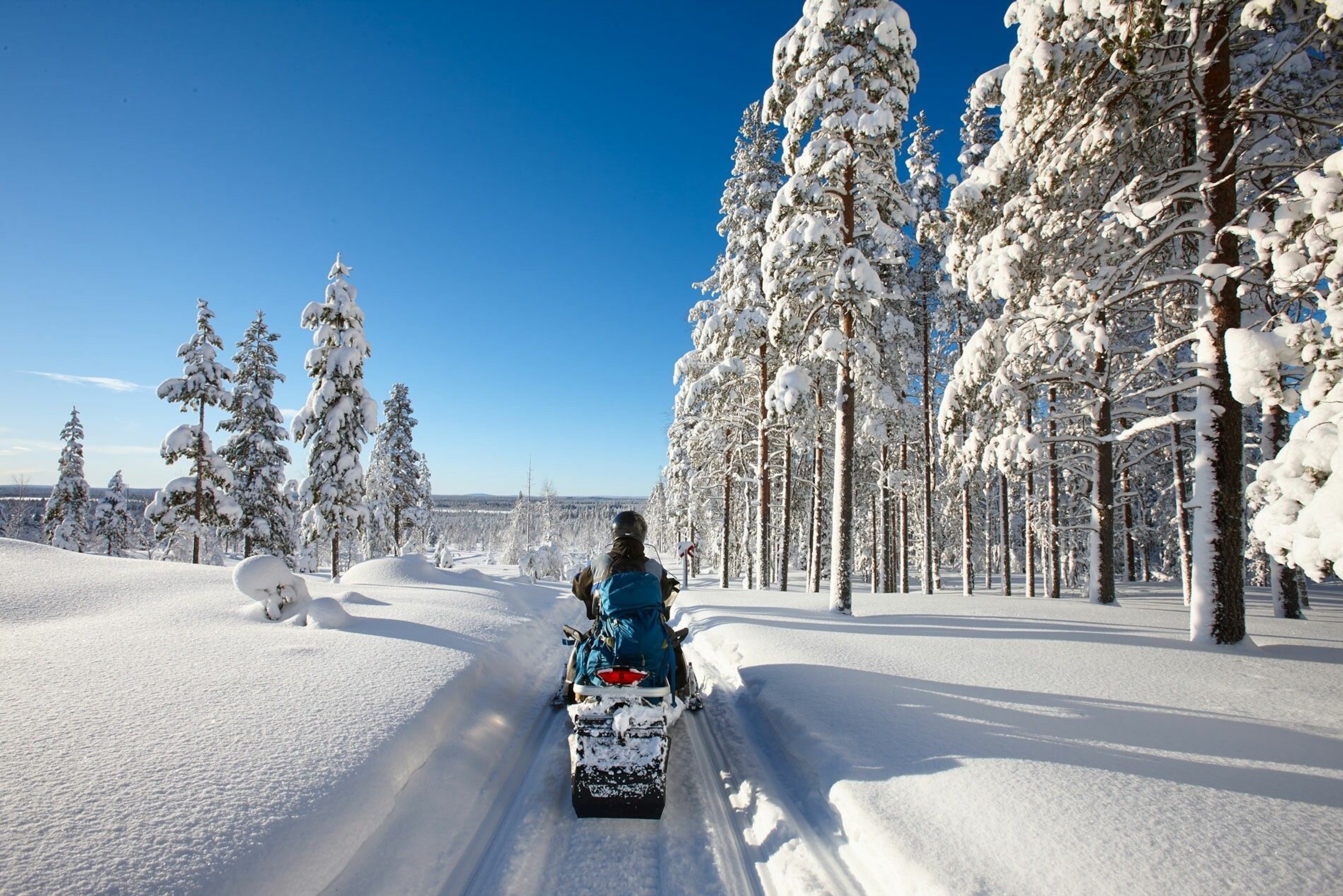 A person riding a snowmobile through a track between two snow banks.