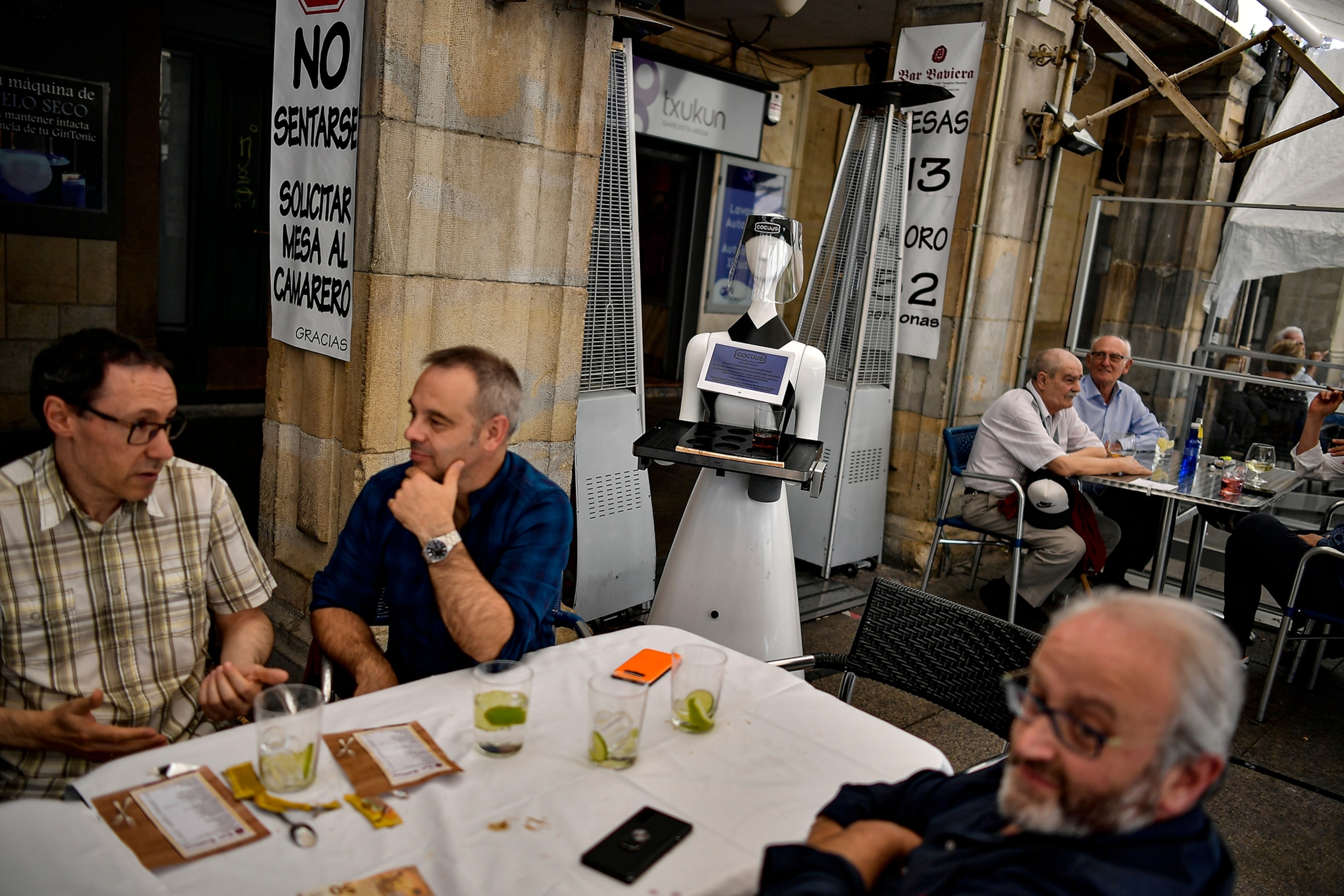 men around table and white robot with a tray serving them.