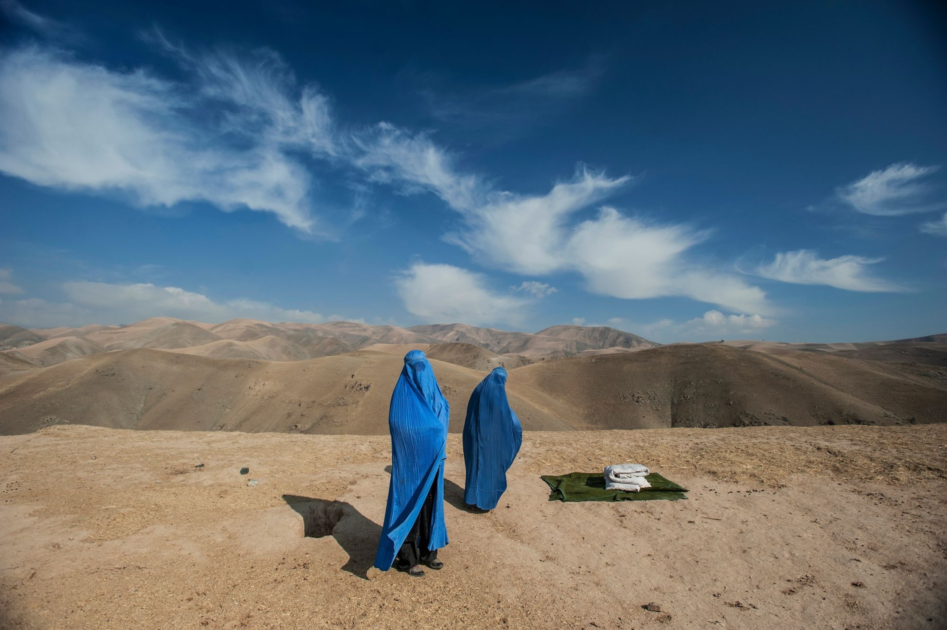 Two women in blue in a vast, bare mountain landscape