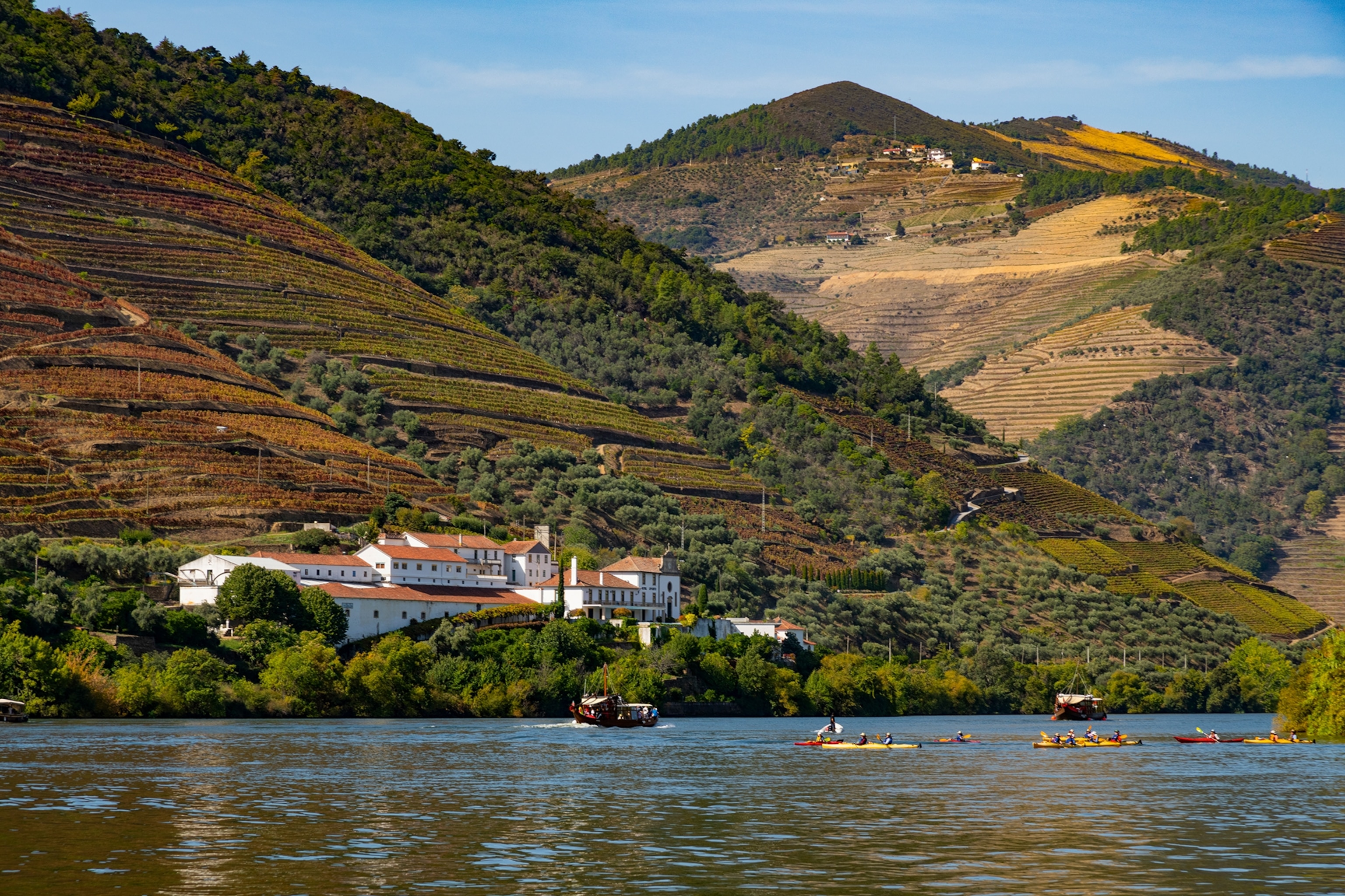 A multi-layered hilly landscape with a river running in front, multiple kayakers are in the water.