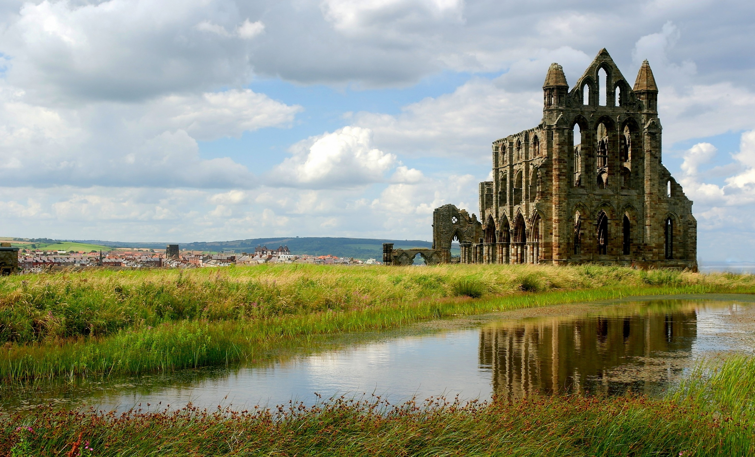 Ruins of an abbey stand in the background reflected in a puddle on the ground