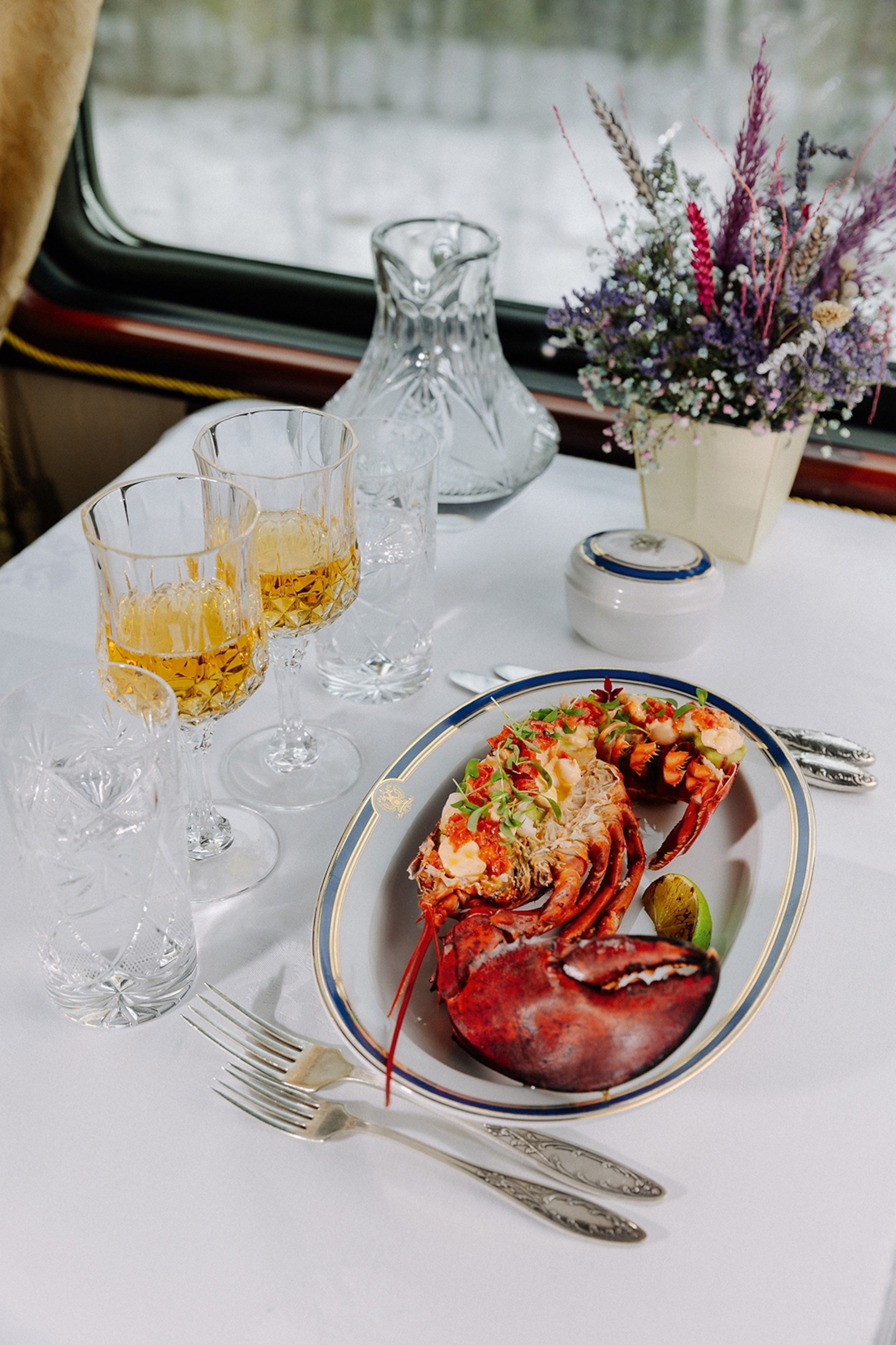 A fancy dinner table set with two sets of silver cutlery and a plate of lobster.