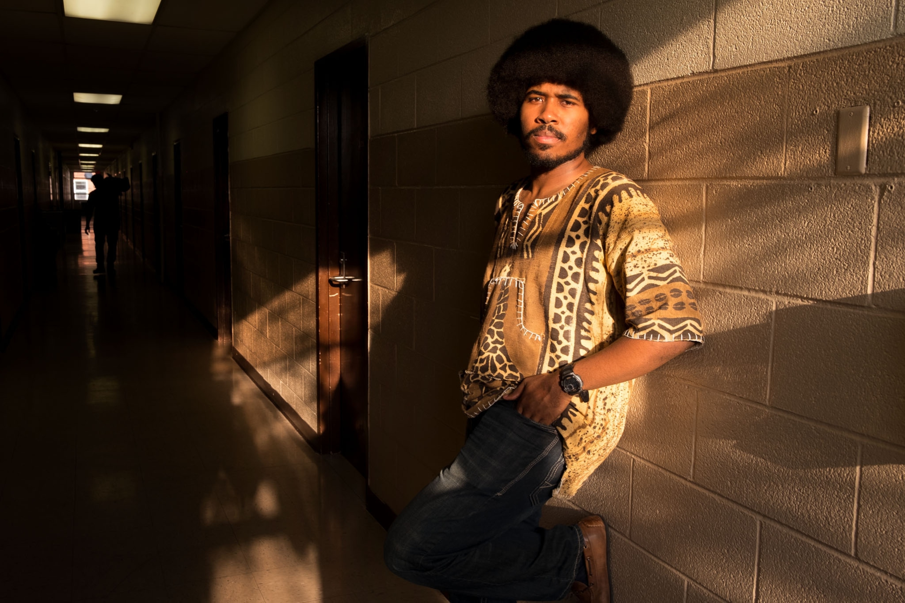 a young black man with an afro in a patterned shirt during sunset in a school hall