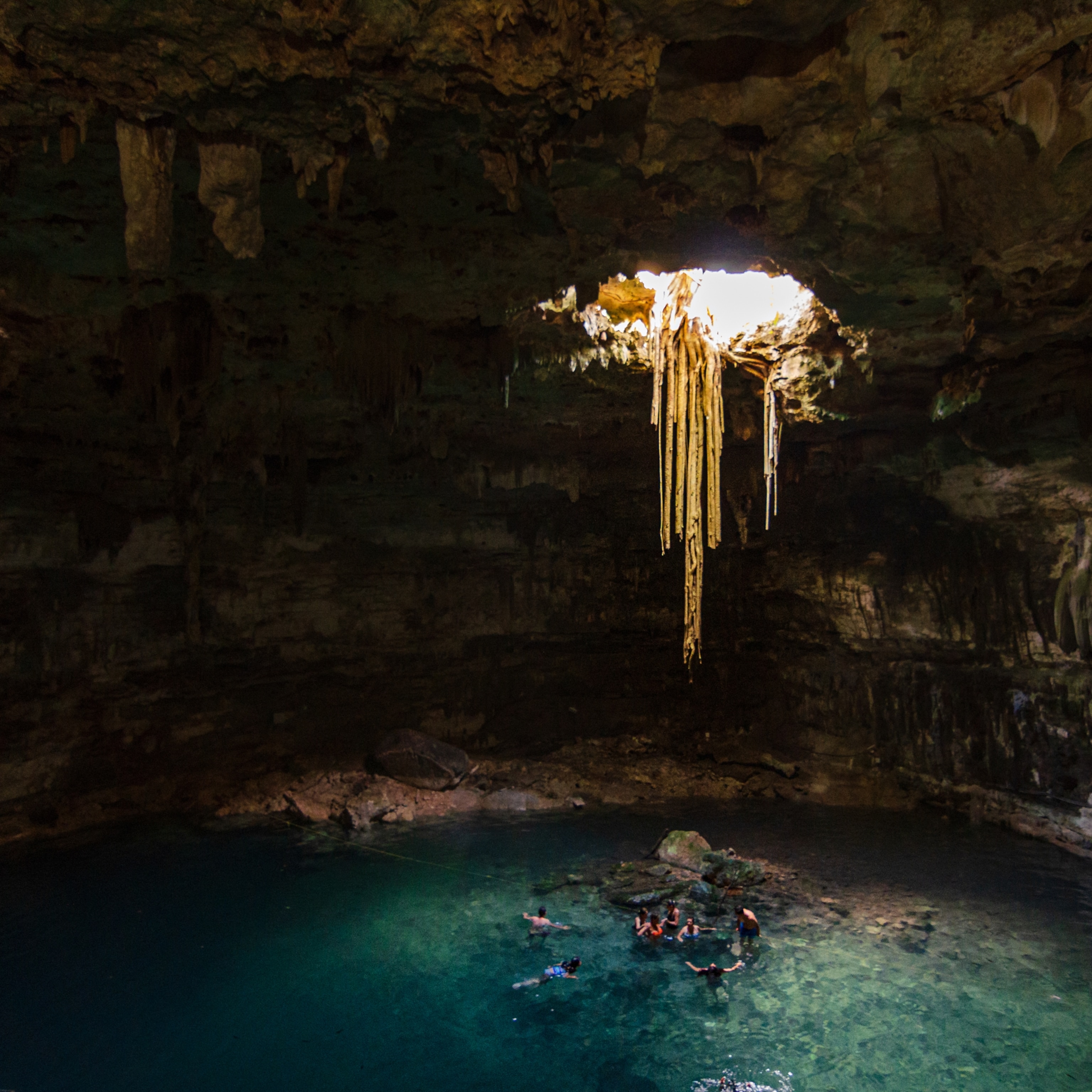 People Swim in waters of a cave, single hole in ground lets light in