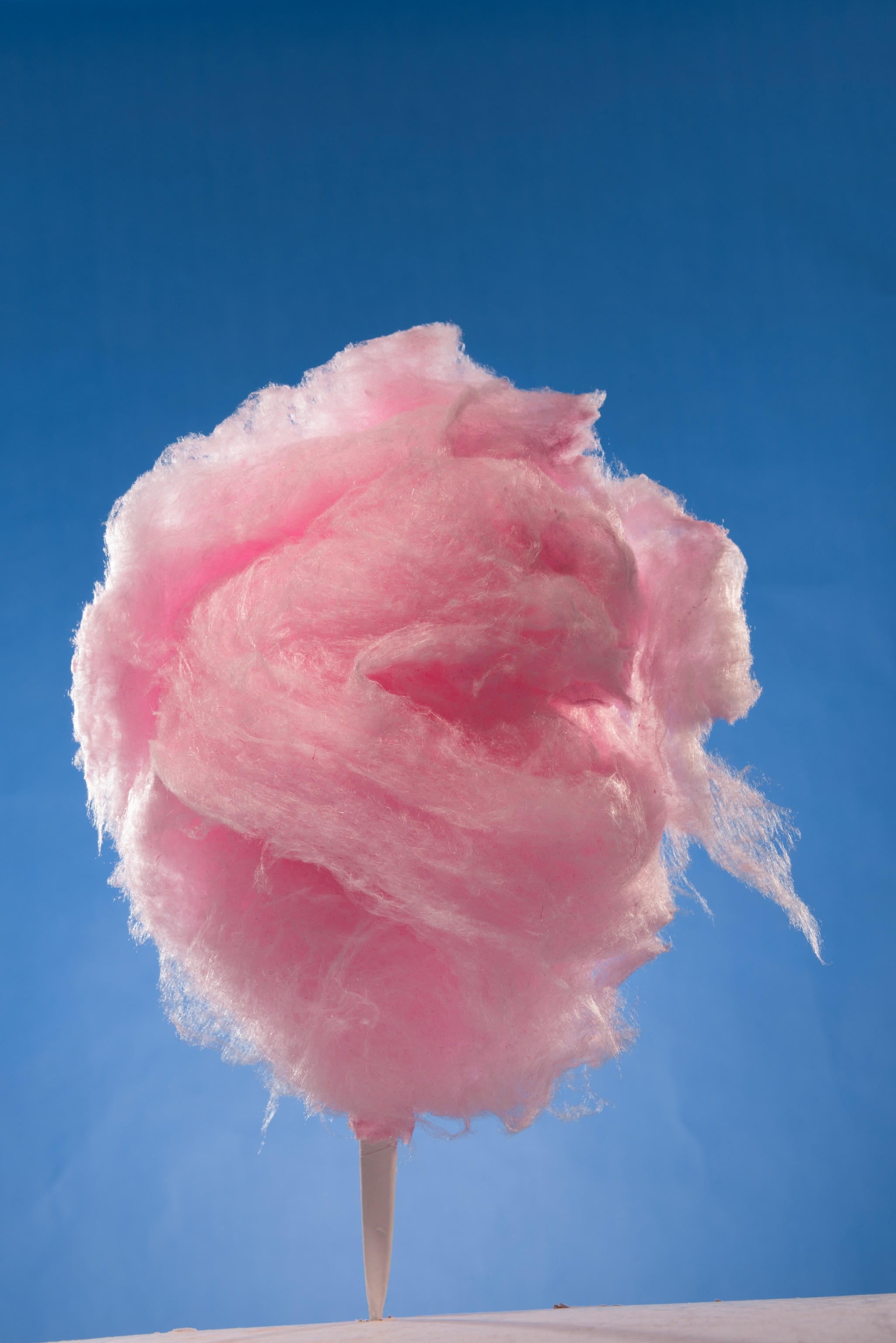 A stick of pink cotton candy photographed against a clear, blue, sky.