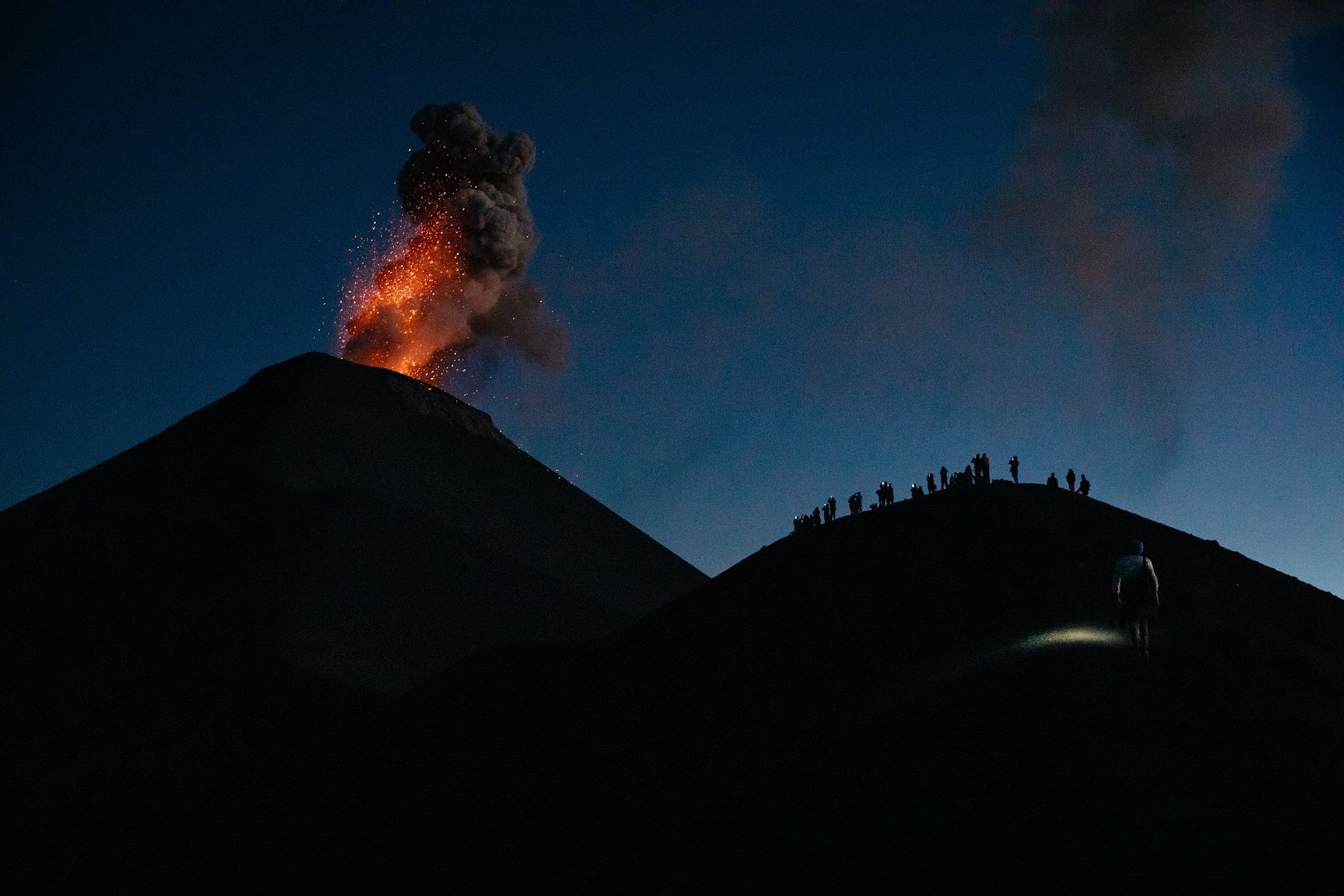 Hikers gather on top of Volcán de Fuego to watch an eruption as the sun sets.