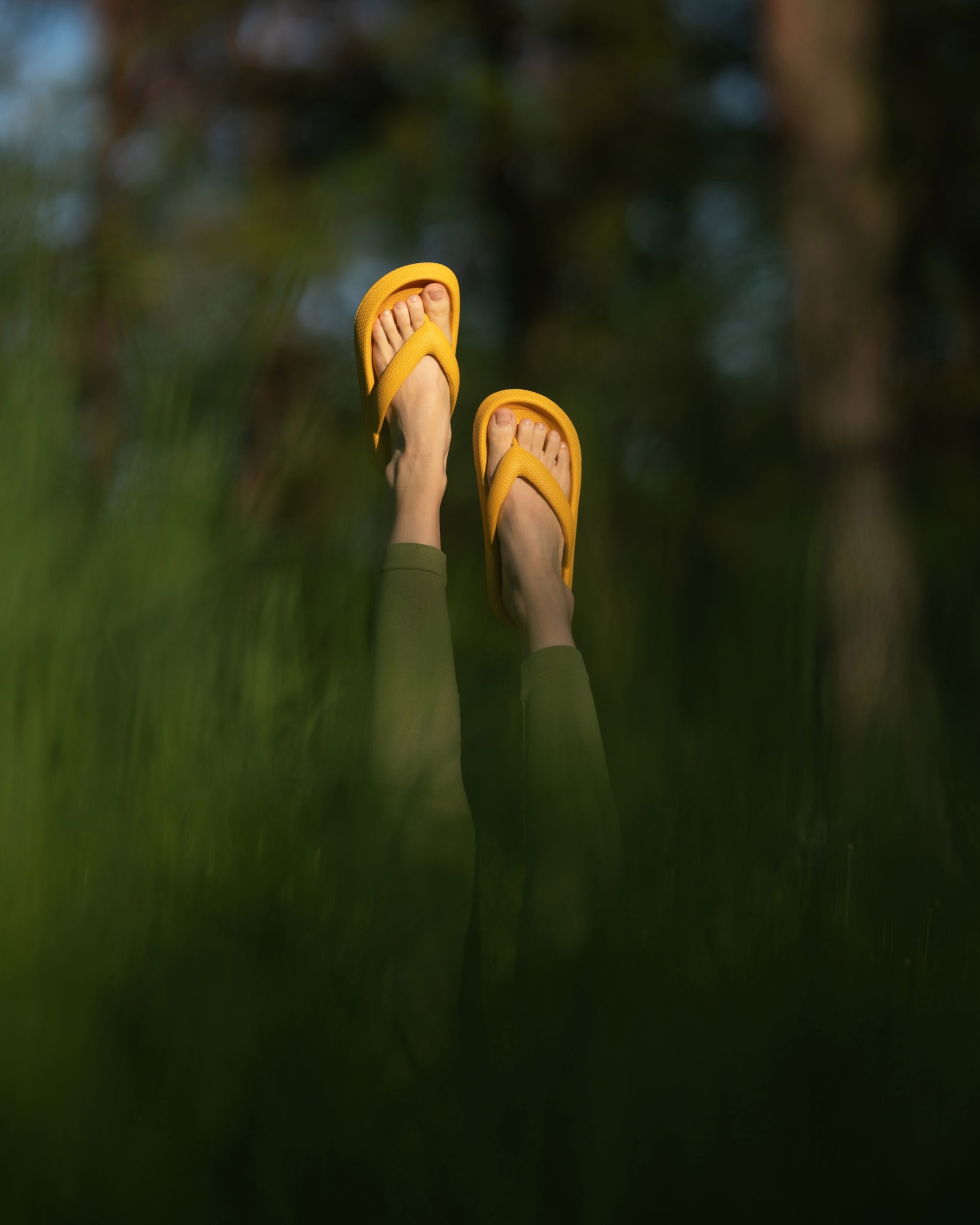 Yellow summer slippers on women's feet outside in the grass in summer. Flip-flops leisure and home shoes. Women's shoes. Front view. Green background. High quality photo