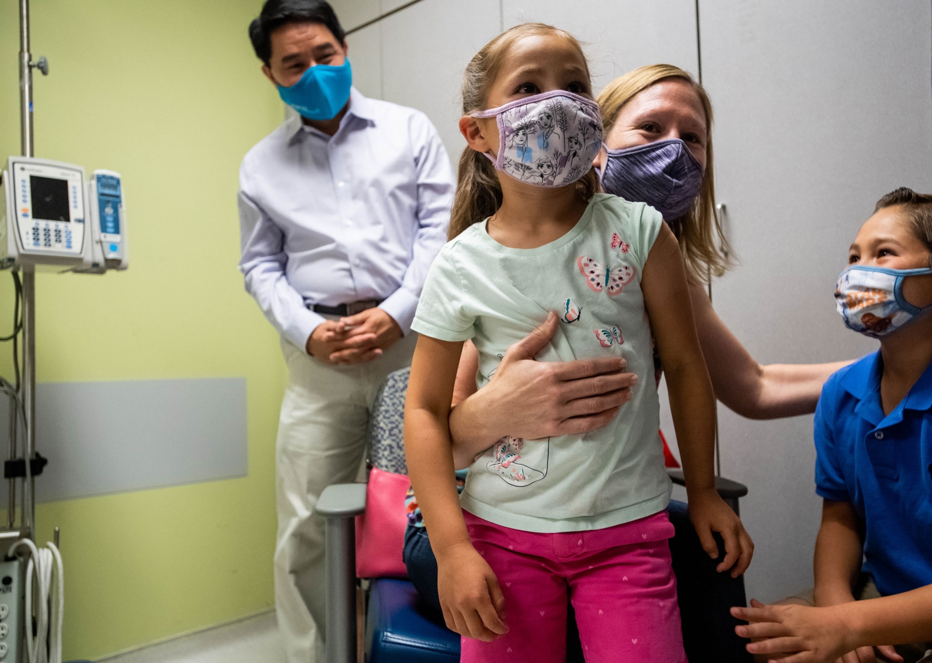 In a medical office, mother hugs her children who are smiling while the father stands in the background.