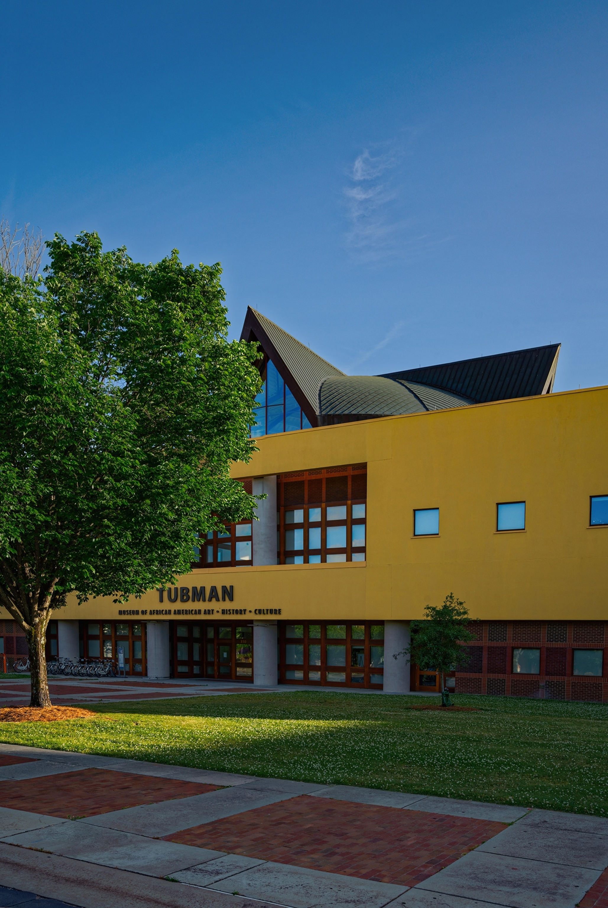 A yellow building with large letters "Tubman" on the front, a manicured lawn and blue sky.