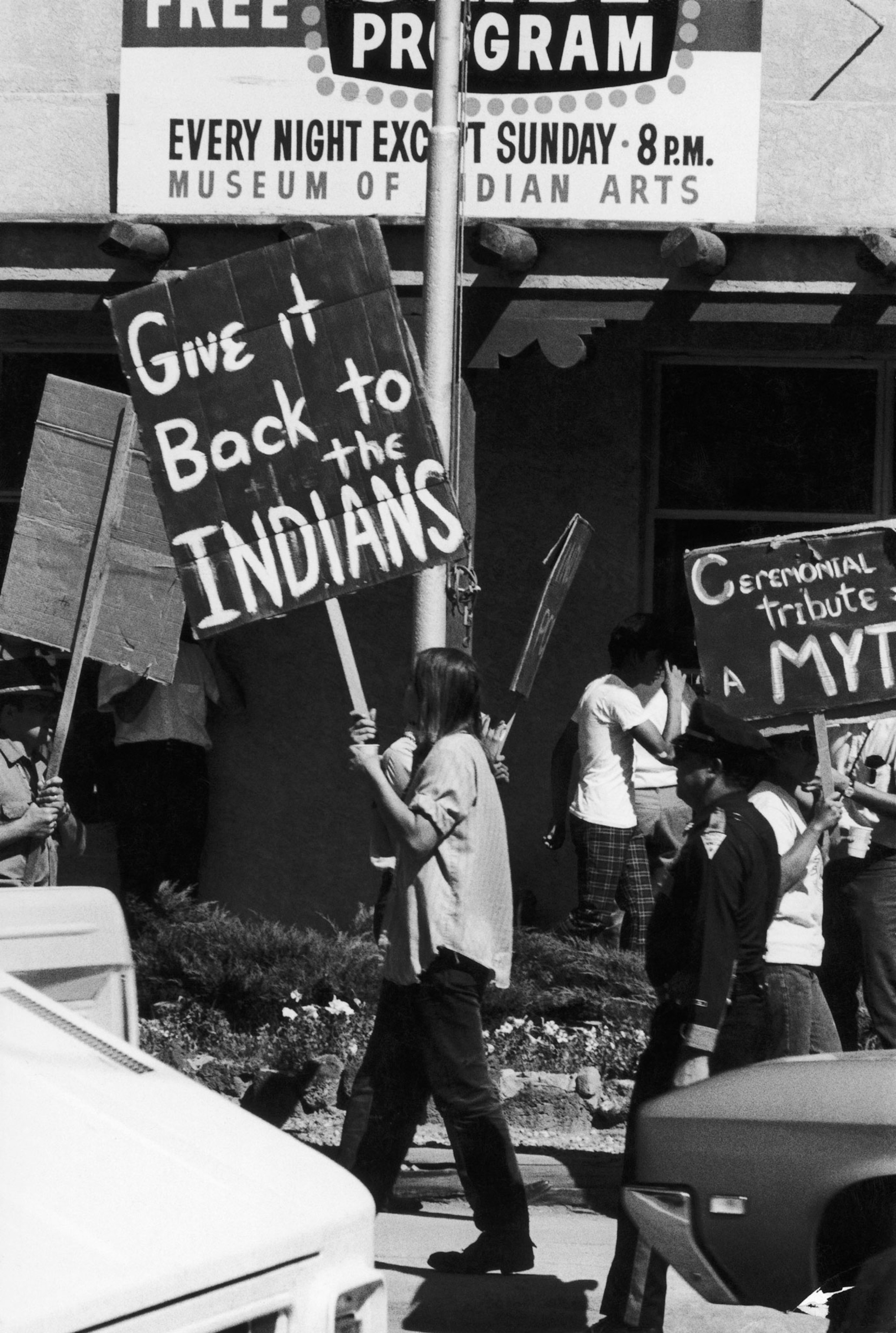 People walk in a picket circle holding signs reading Give it back to the Indians