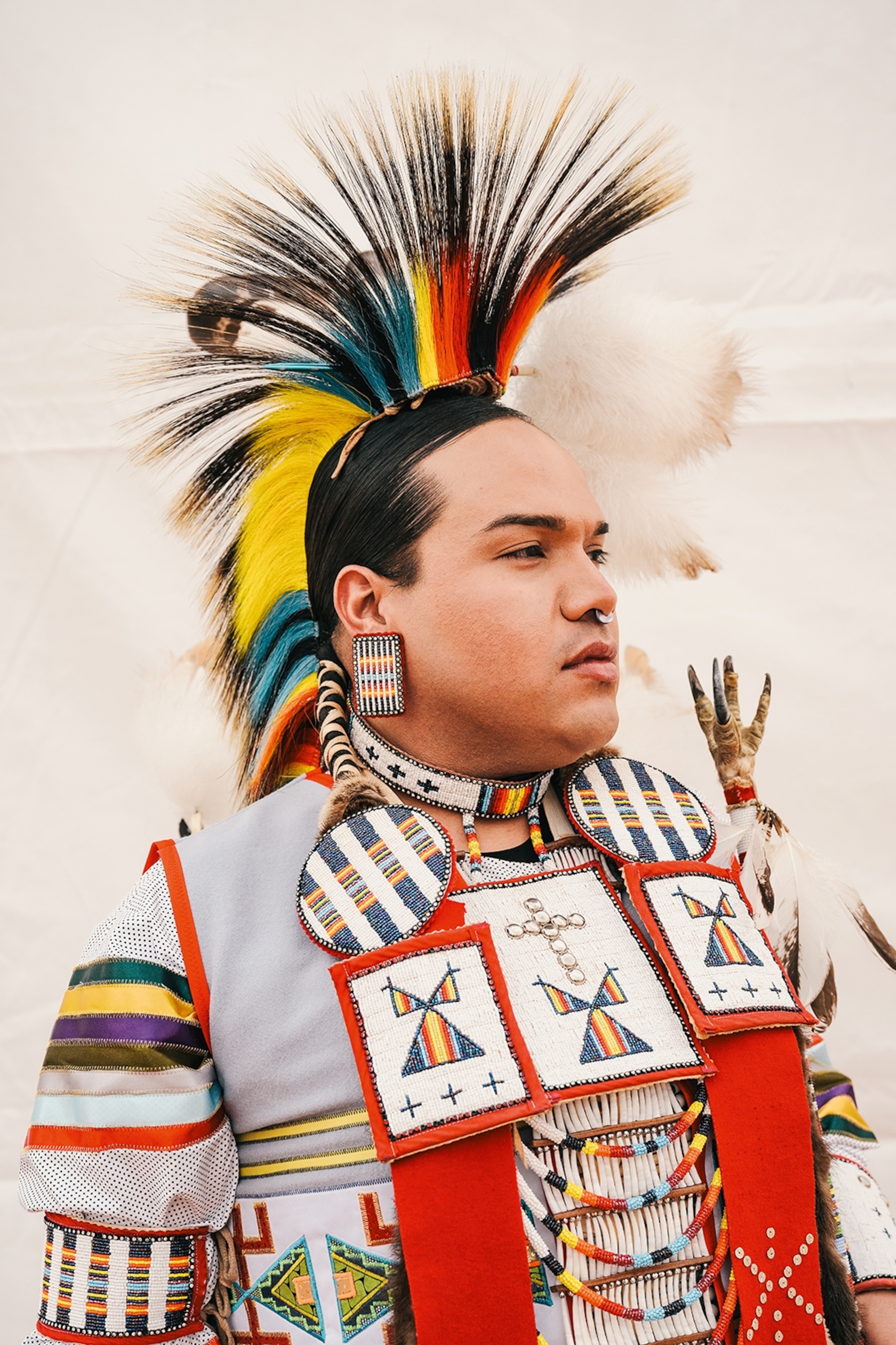 A powerful portrait of a young Native American wearing traditional dress and a feathered mohawk.