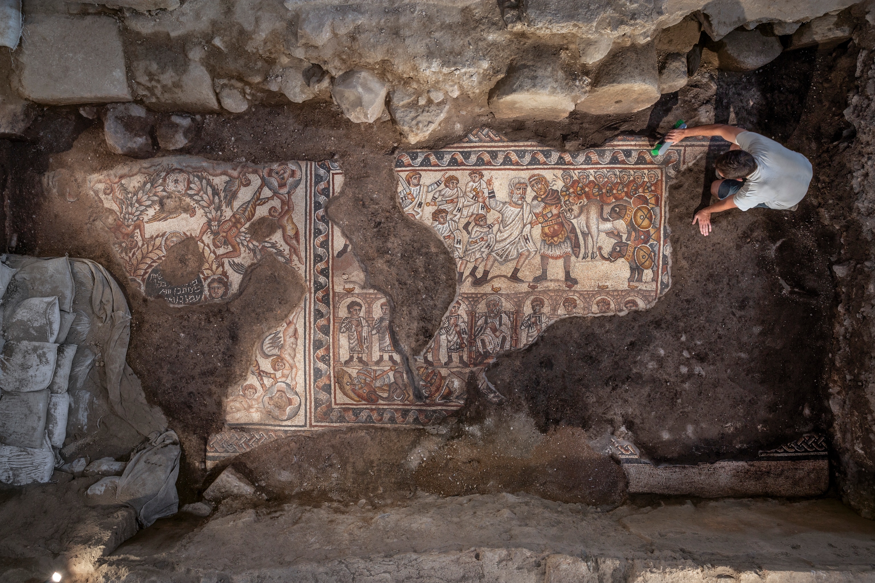 Depicts three horizontal registers (strips) containing human and animal figures, including elephants. The top register, which is the largest, shows a meeting between two men, who perhaps are intended to represent Alexander the Great and a Jewish high priest. A mosaic showing Samson and the foxes. A second mosaic was found that shows Samson carrying the gate of Gaza on his shoulders.