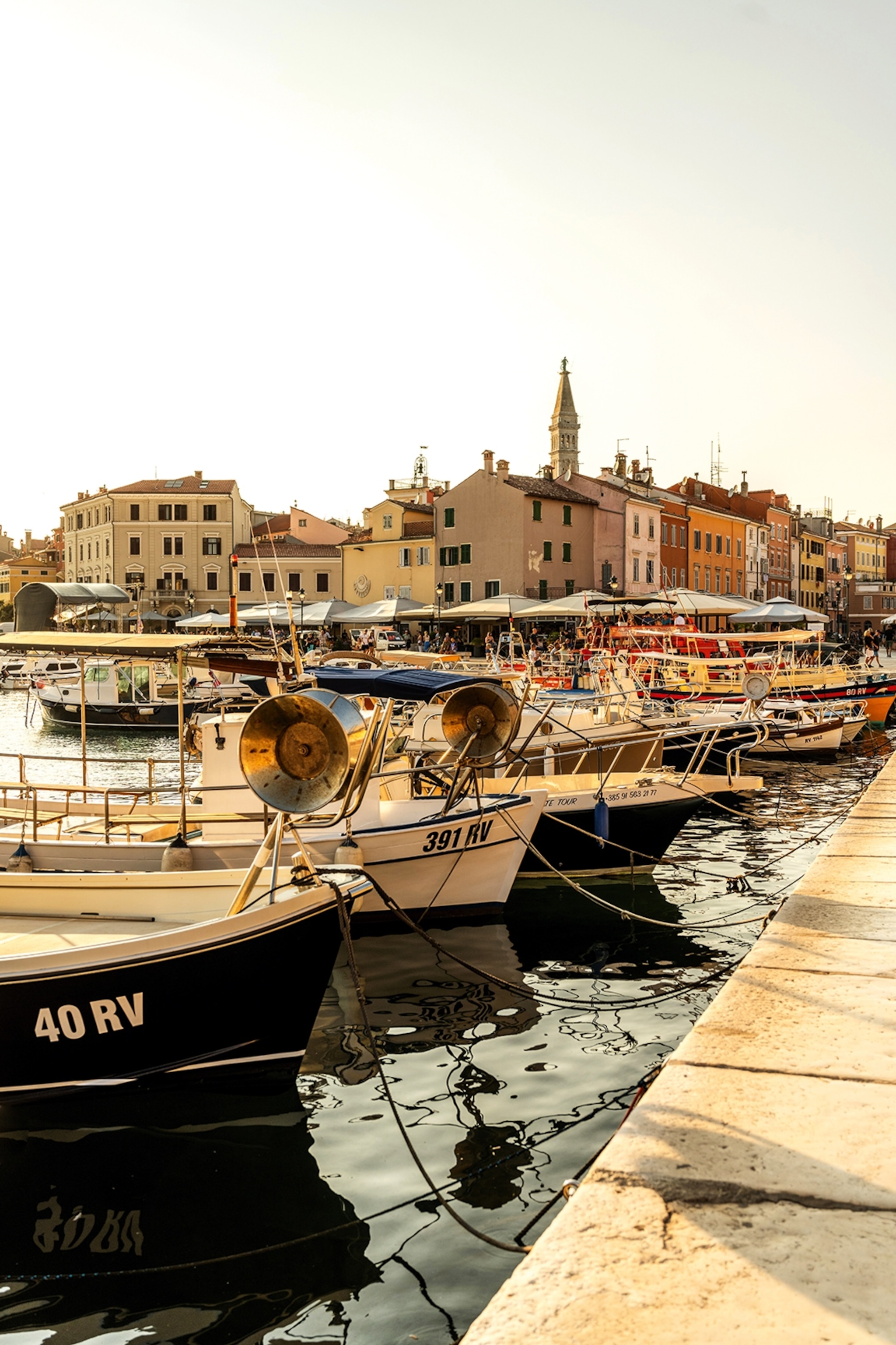 Port of Rovinj, with a charming view of the city with colourful buildings in the distance, and boats lined at the dock.