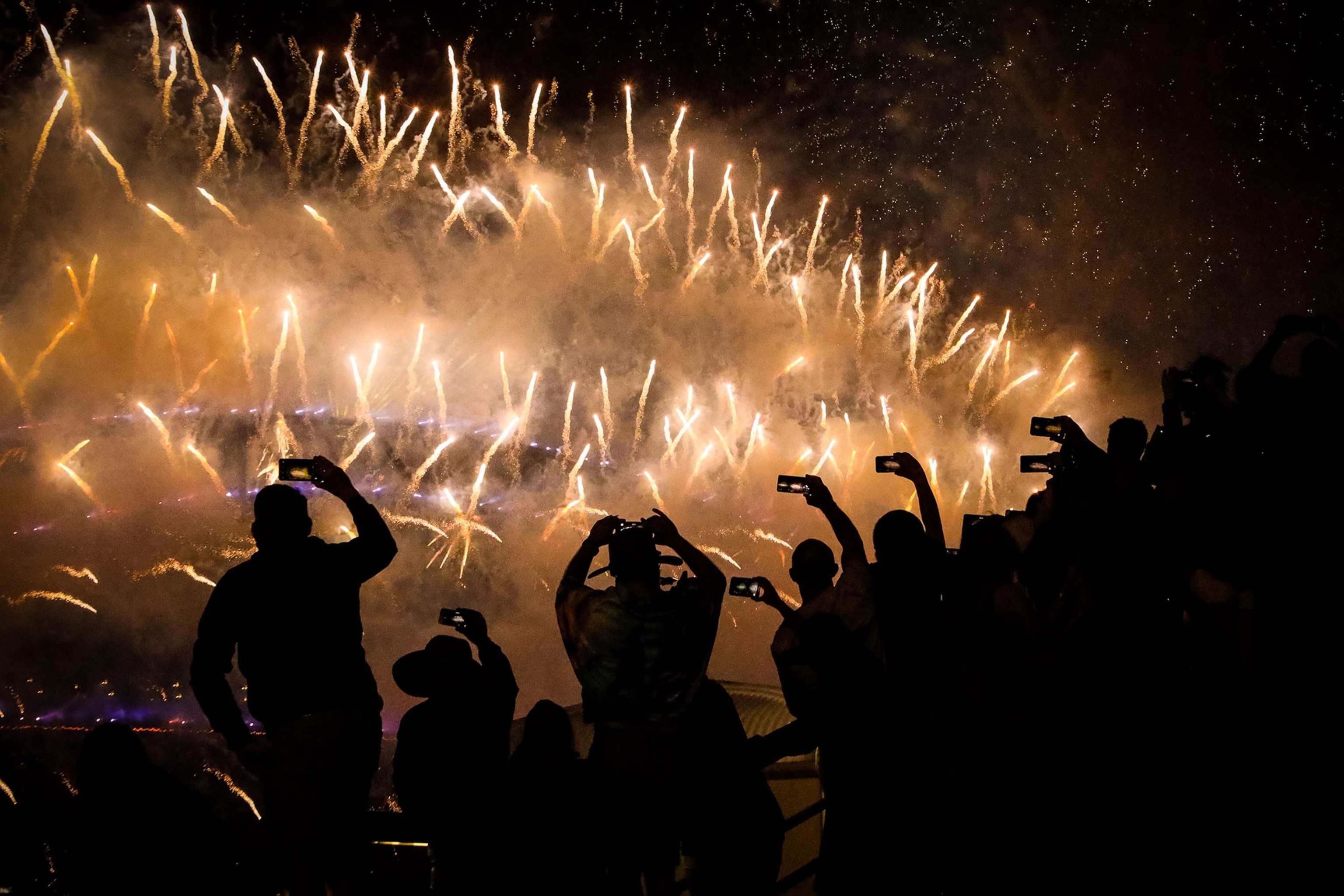 Silhouetted bodies photograph golden firework lights.