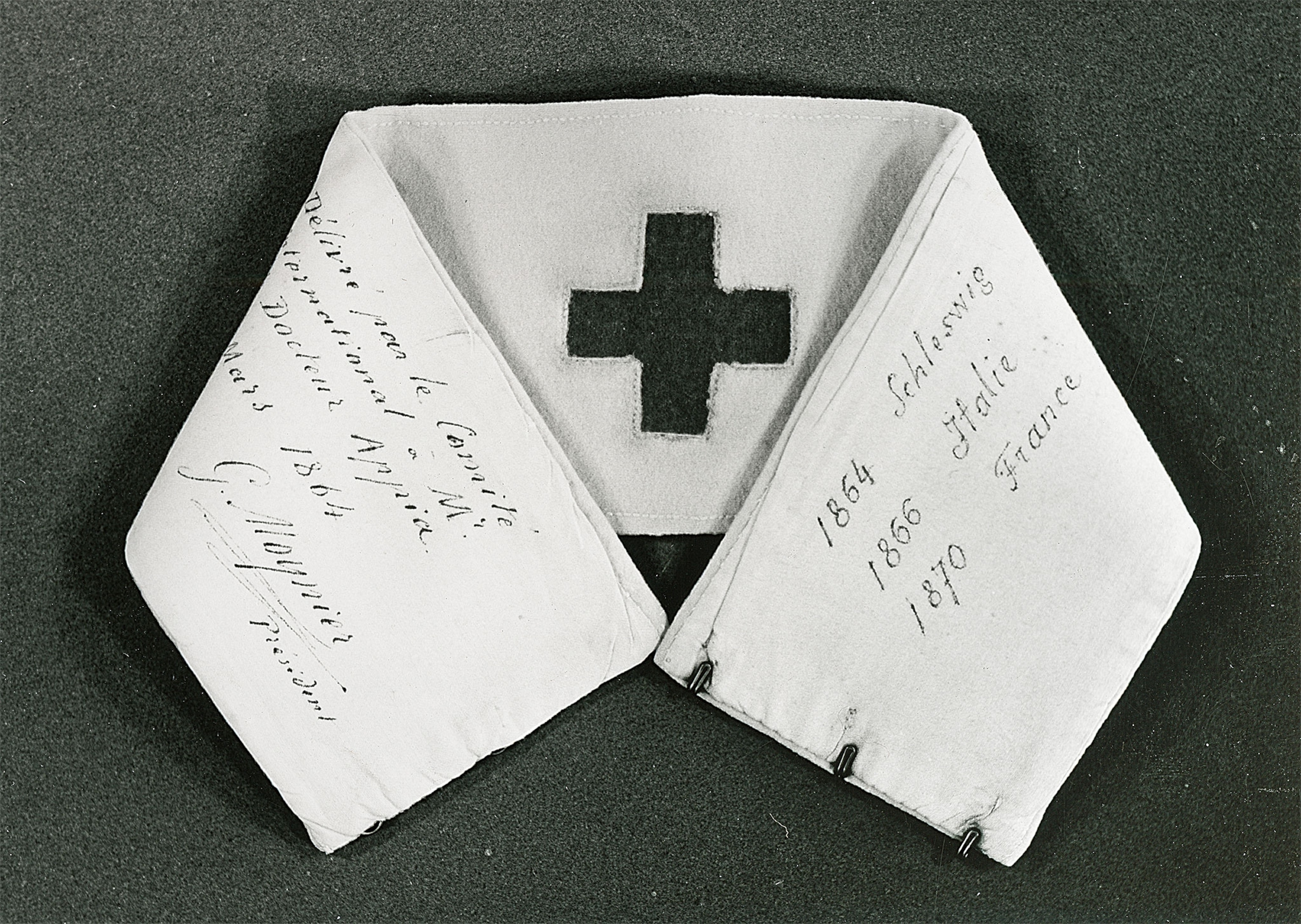 A black and white photo of a white armband folded over with a cross in the middle