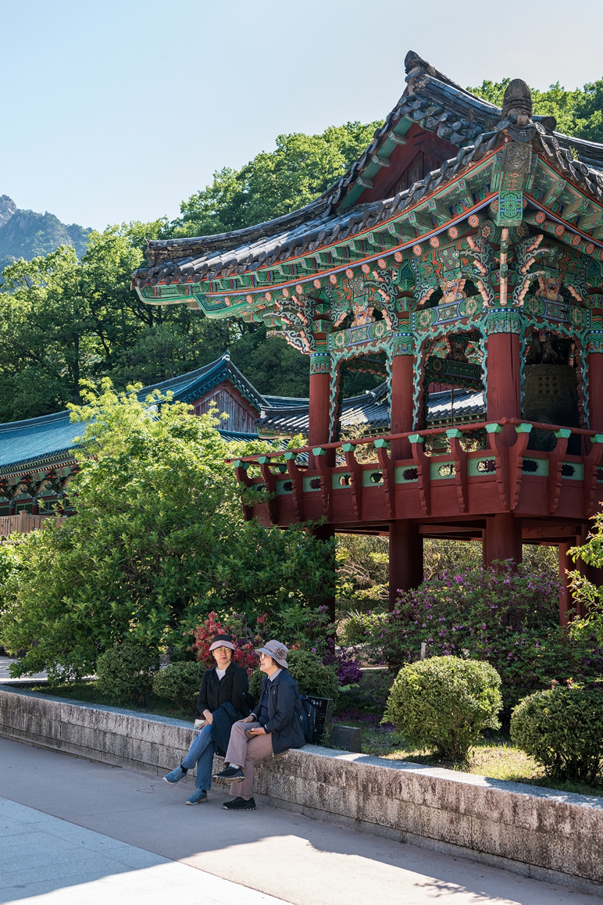 Two women sat on a low wall underneath an elaborate temple