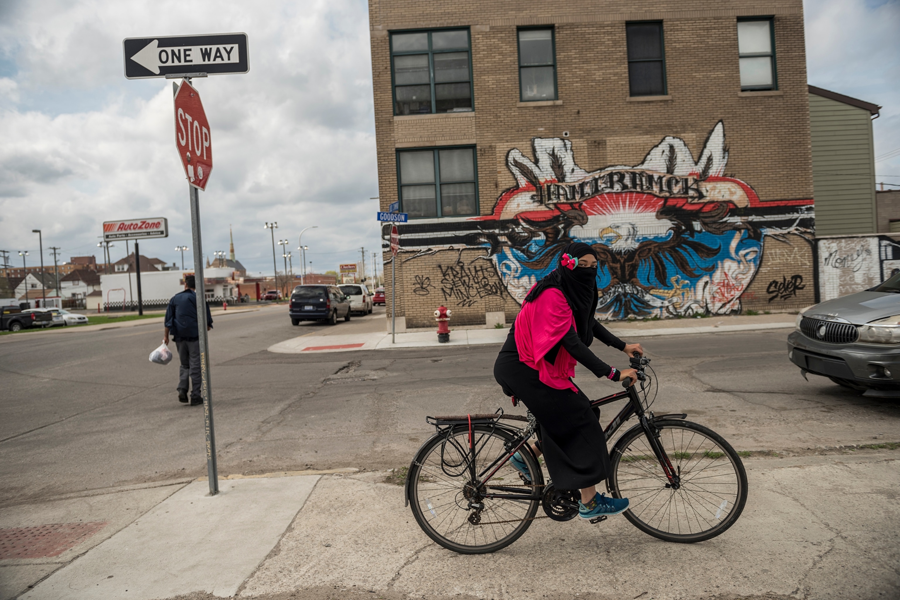 a hijabi woman wearing pink and black riding a bicycle in front of a graffiti wall
