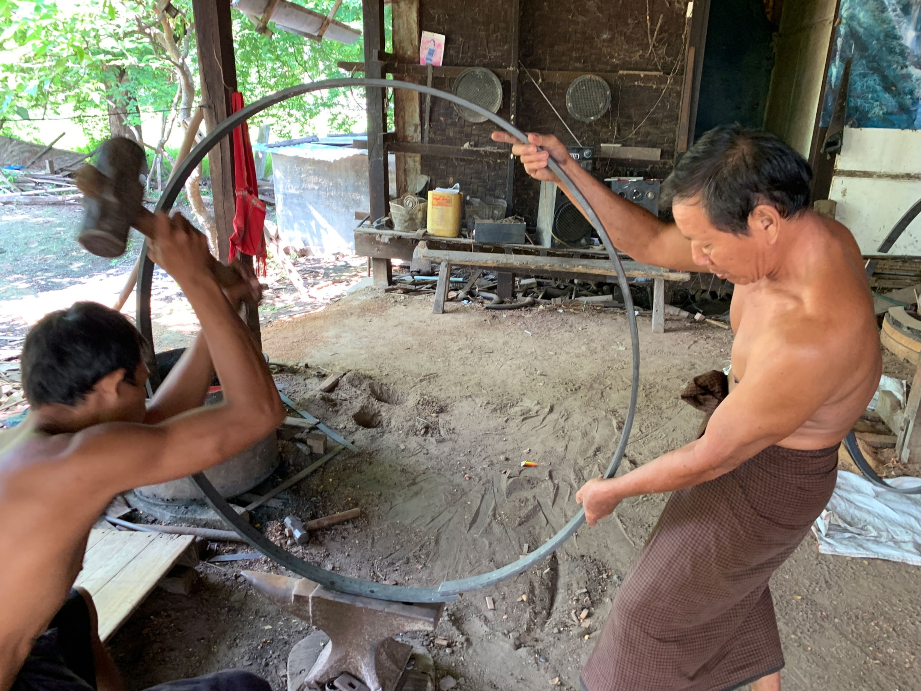 Two men bend a metal bar into a circle