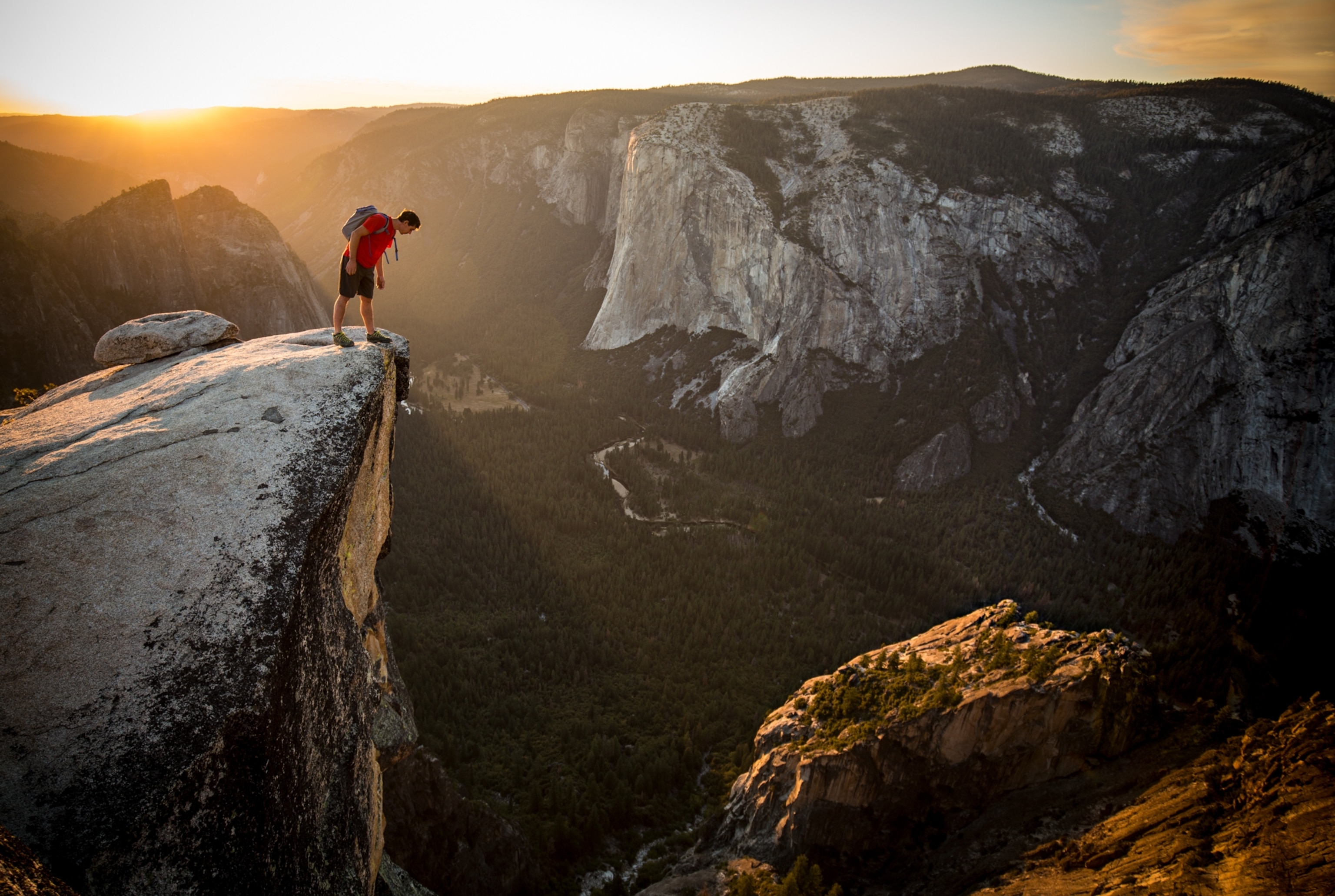 a man in red shirt looking down over cliff edge
