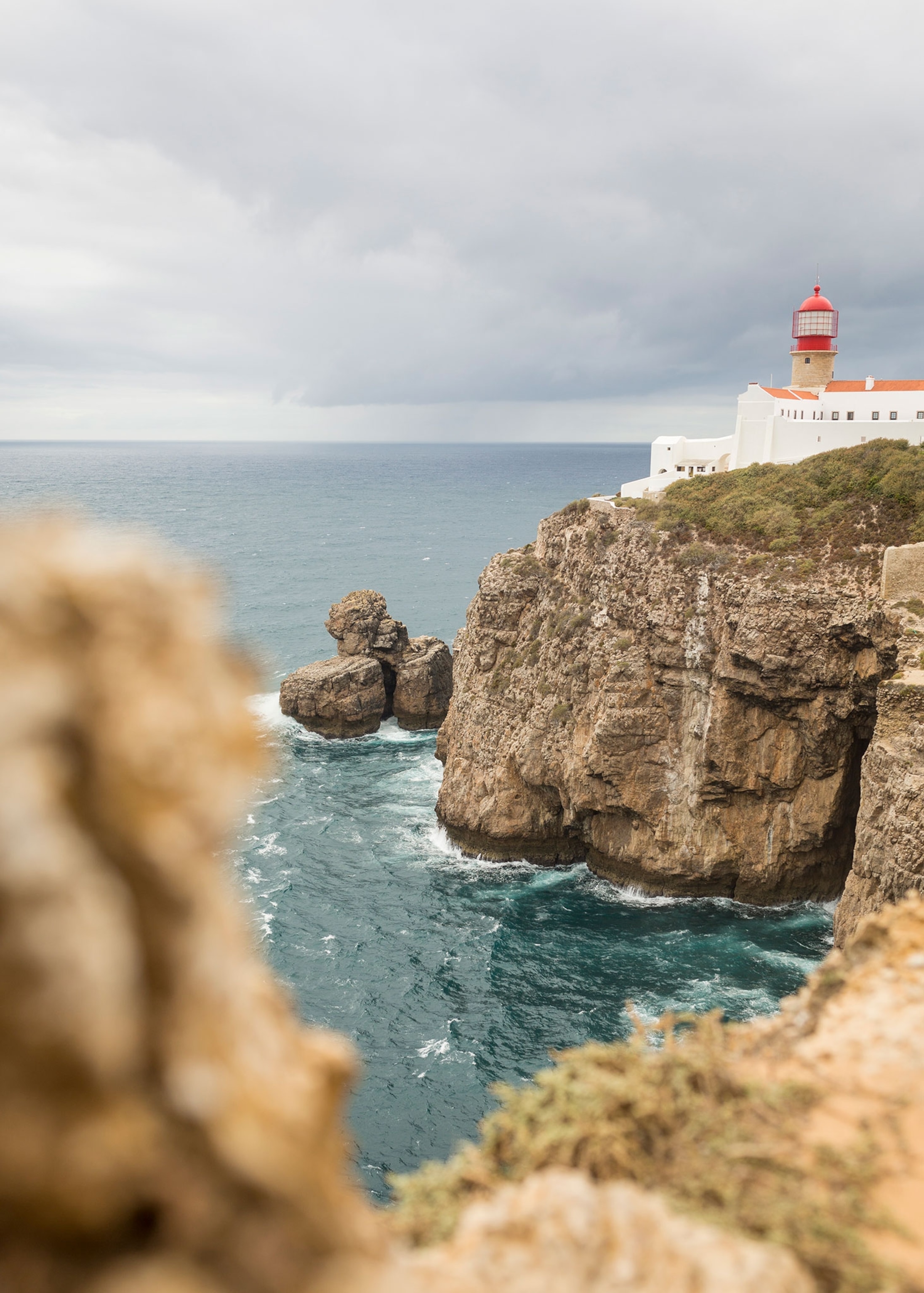 Rocky cliffs sit to the right of a blue ocean with a light house at the edge of the rocks.