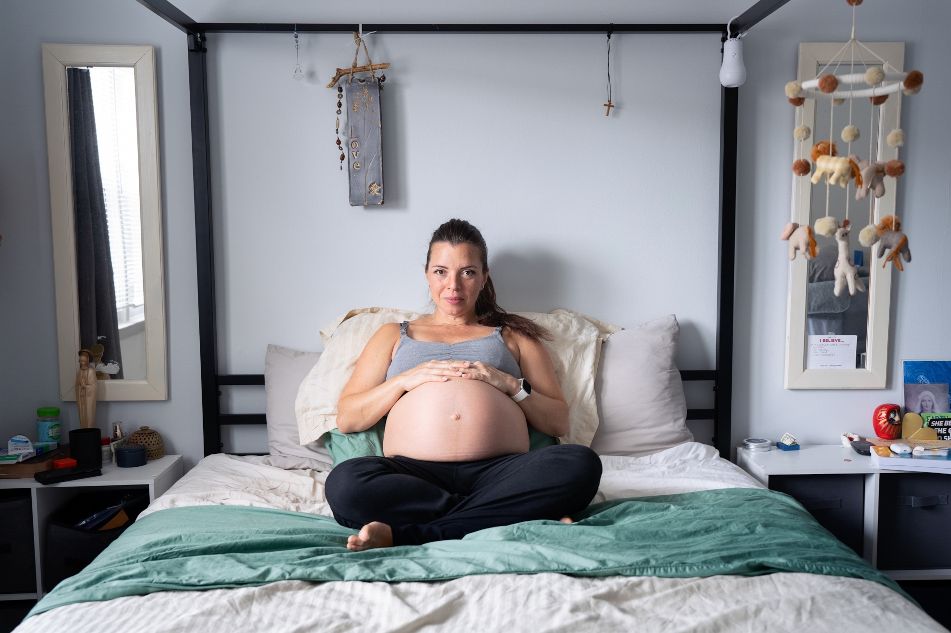 Allison sits in bed with her hands resting on her pregnant belly.