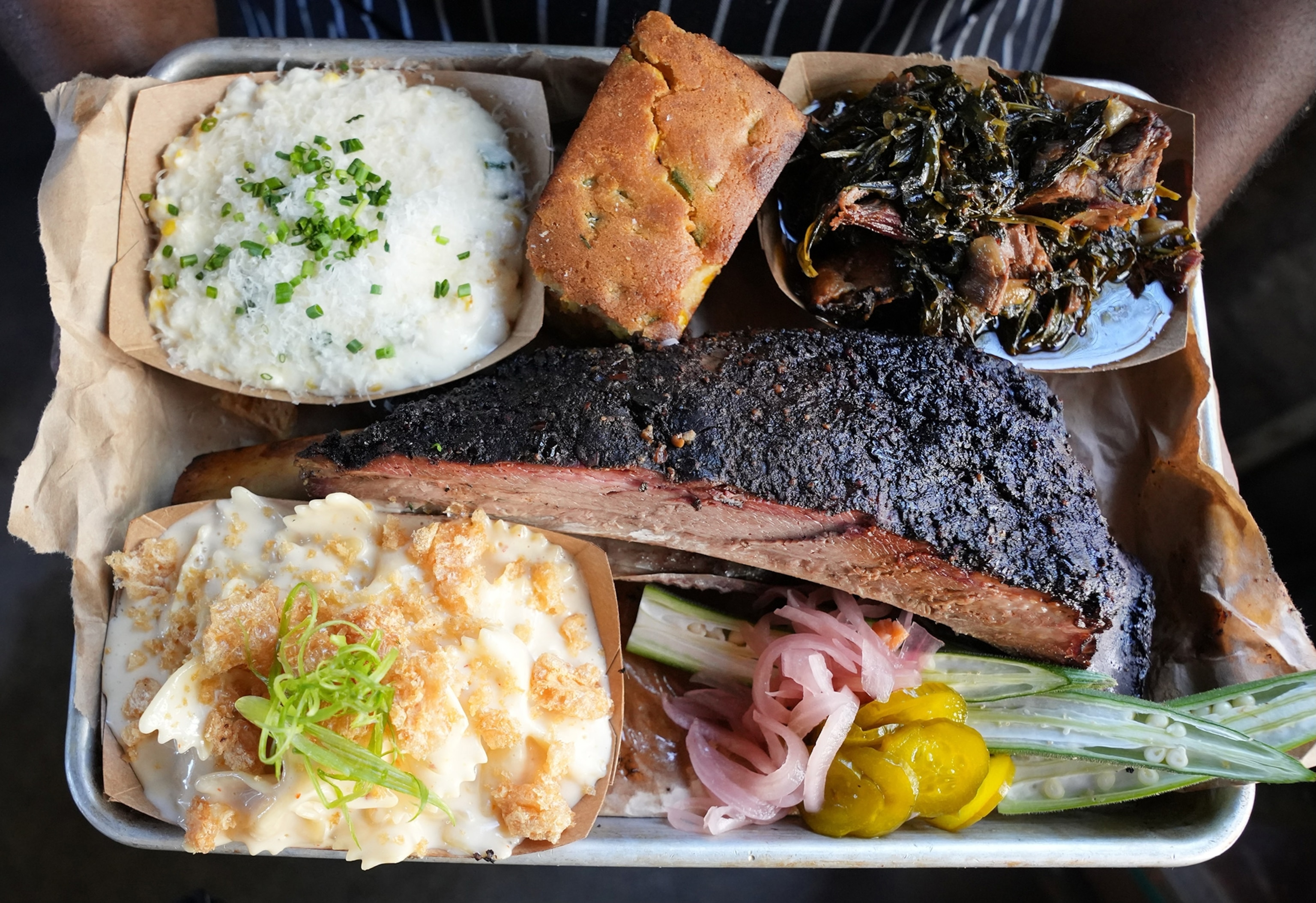 Smoked Beef Short Ribs with Cheese Grits, Mashed Potatoes with pork cracklings, greens, our seasonal escabeche and pickles, and house made jalapeño cornbread on a tray.