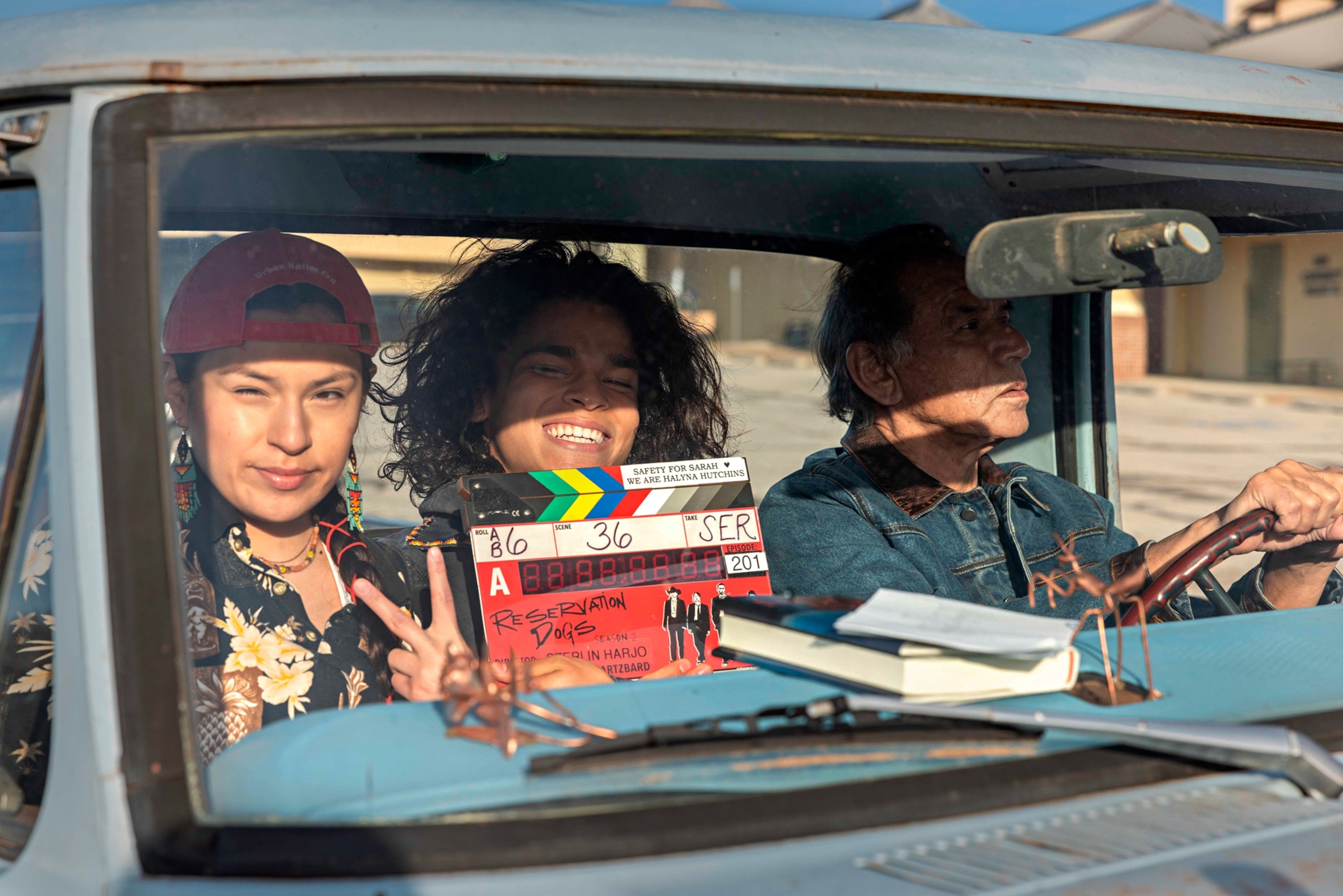 Driver and two your person displaying clapperboard with Reservation Dogs written on it.